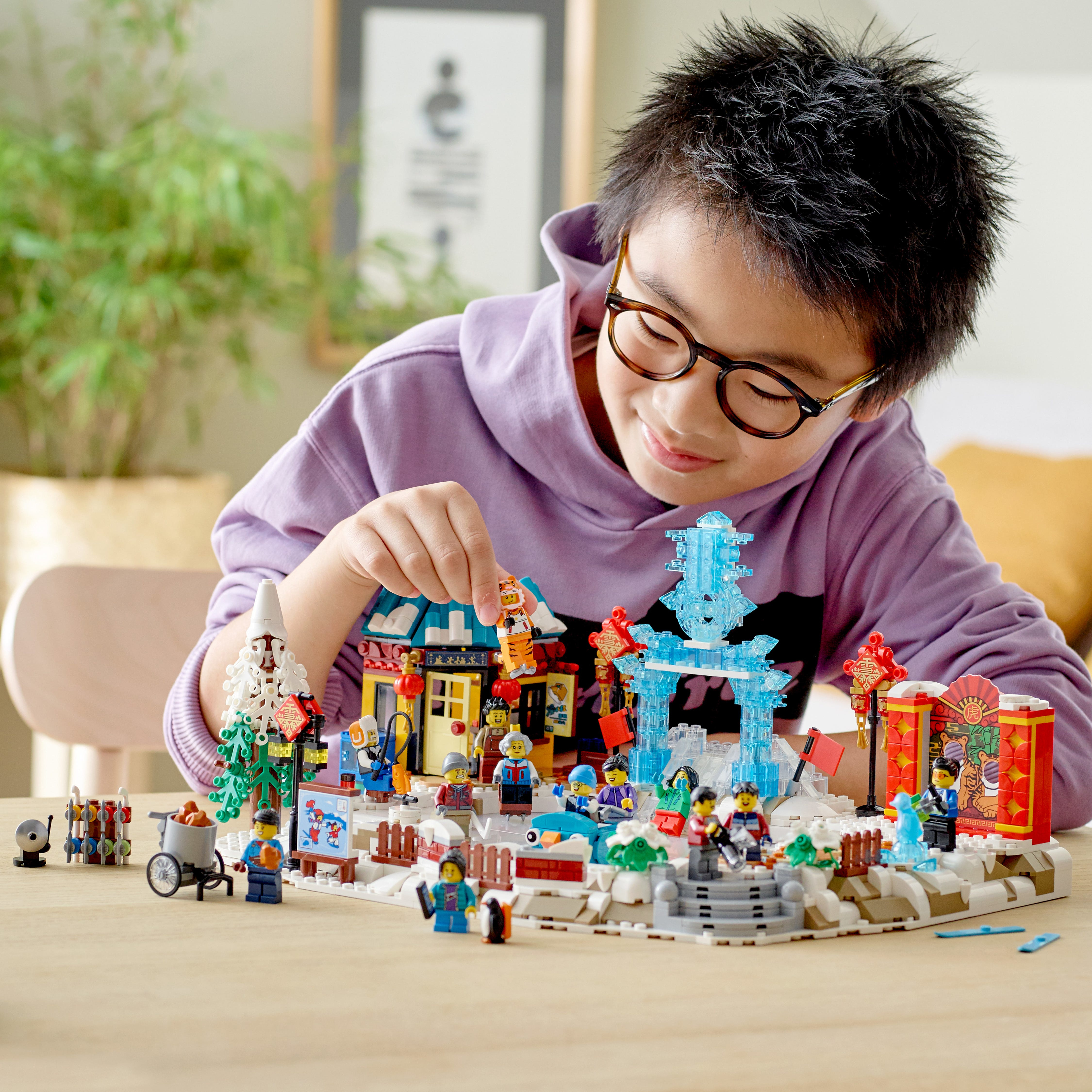 Un bambino con gli occhiali gioca con un set LEGO del festival invernale, circondato dagli elementi del set.