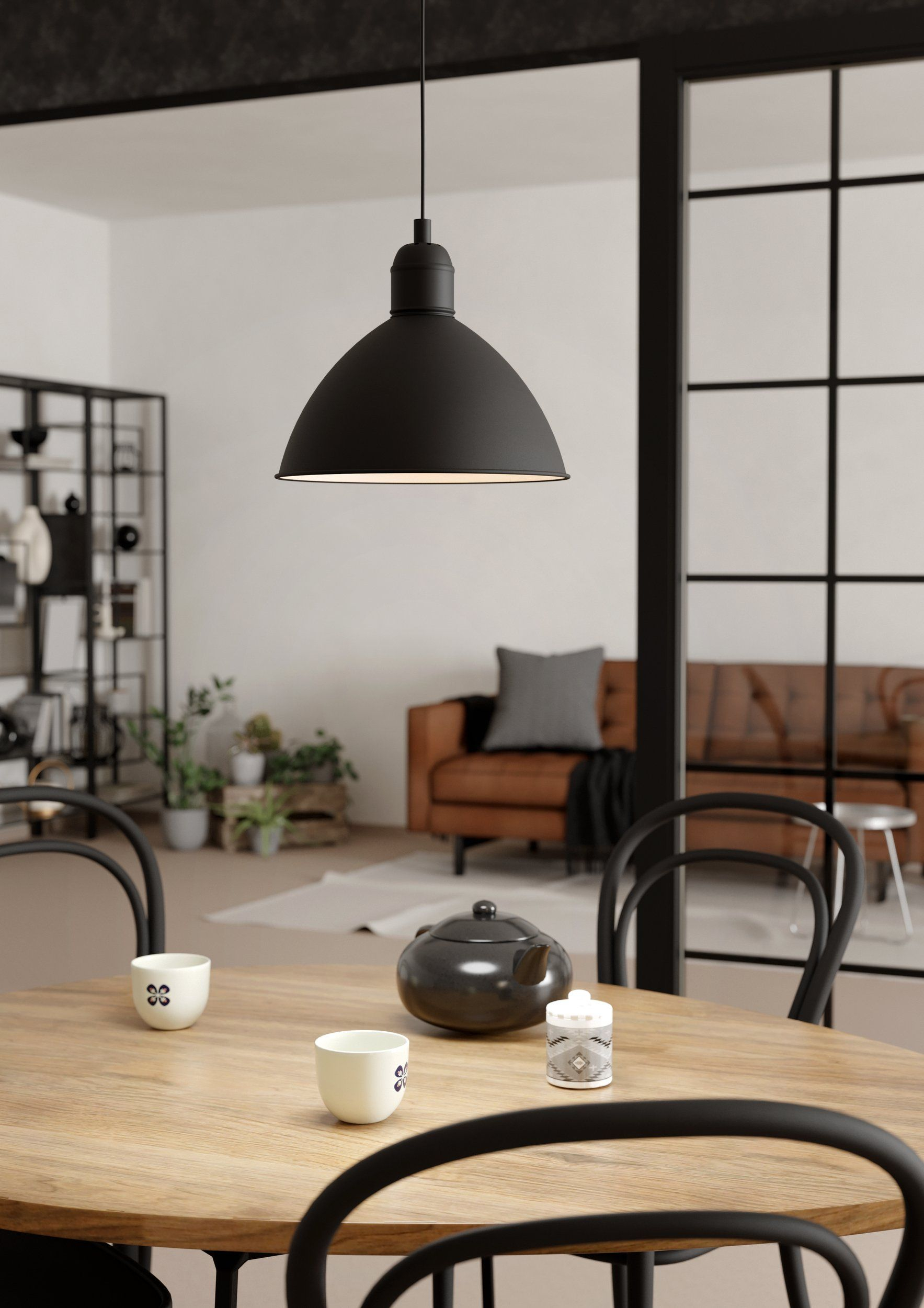 Una lampada a sospensione nera pende su un tavolo di legno con accessori per il tè, creando un'atmosfera accogliente.
