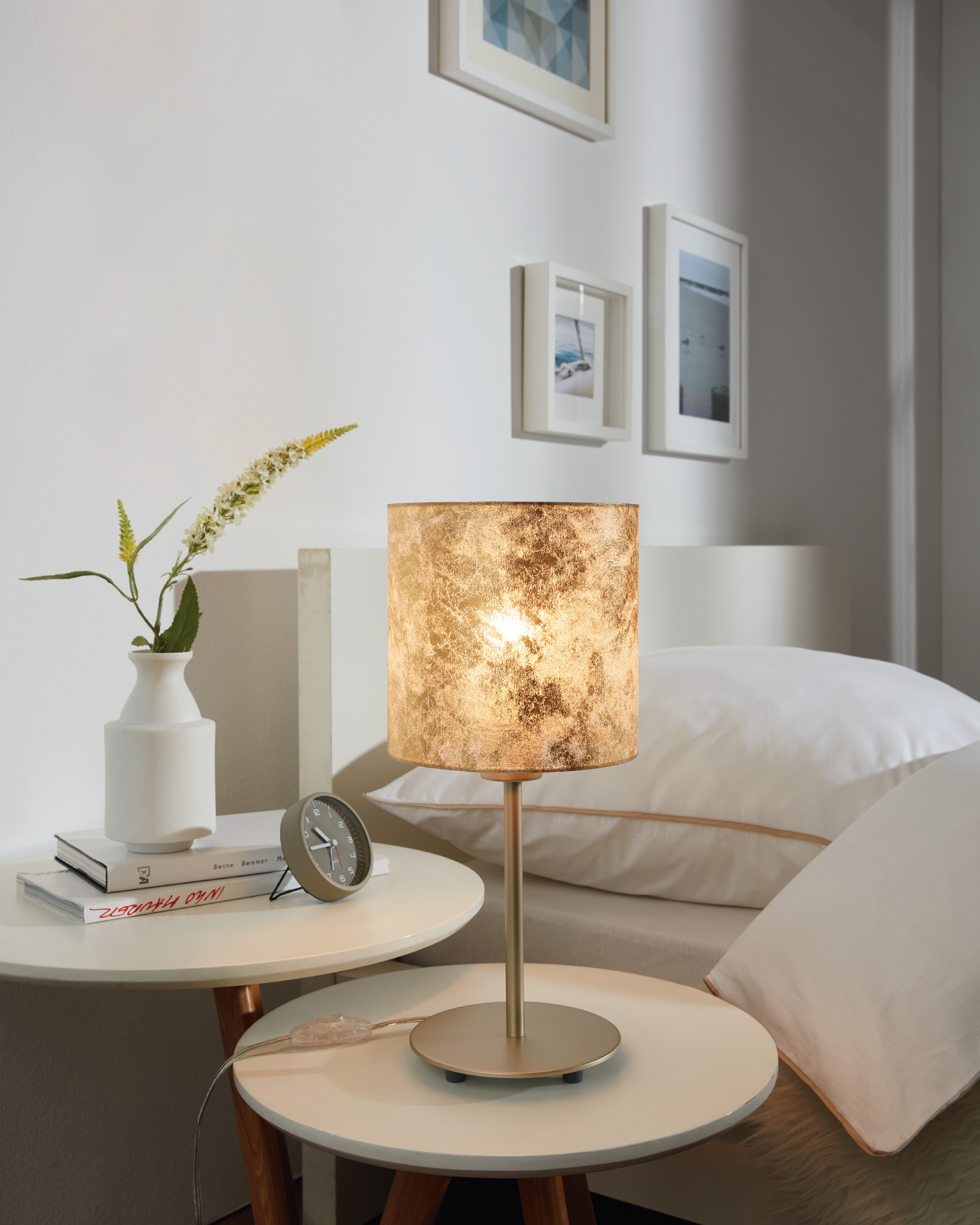 Schlafzimmerszene mit goldener Nachttischlampe, Nachttisch, Büchern, Blume und Uhr.