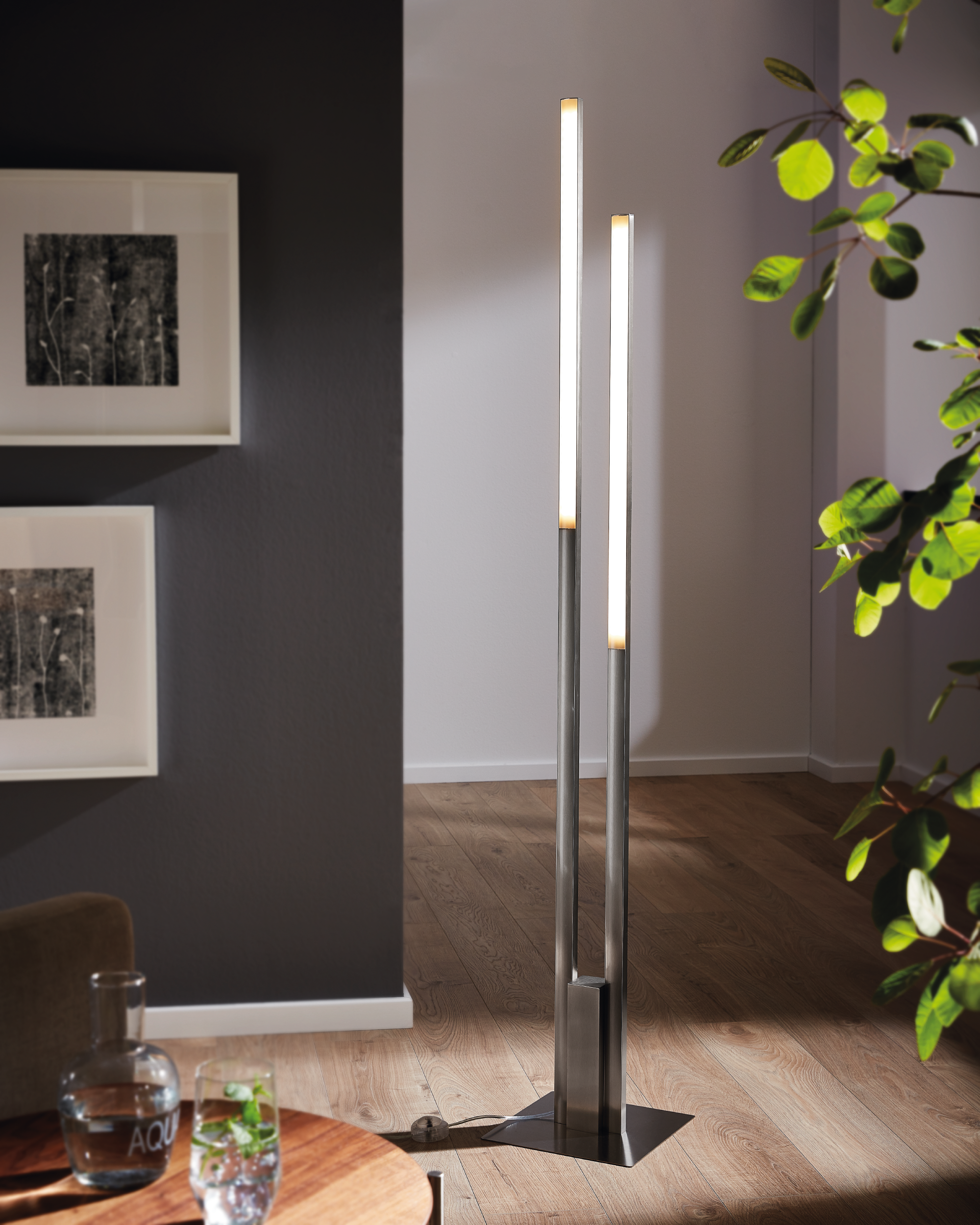 Wohnzimmerszene mit einer modernen Stehlampe mit drei Lichtleisten, einem Beistelltisch und dekorativen Elementen.