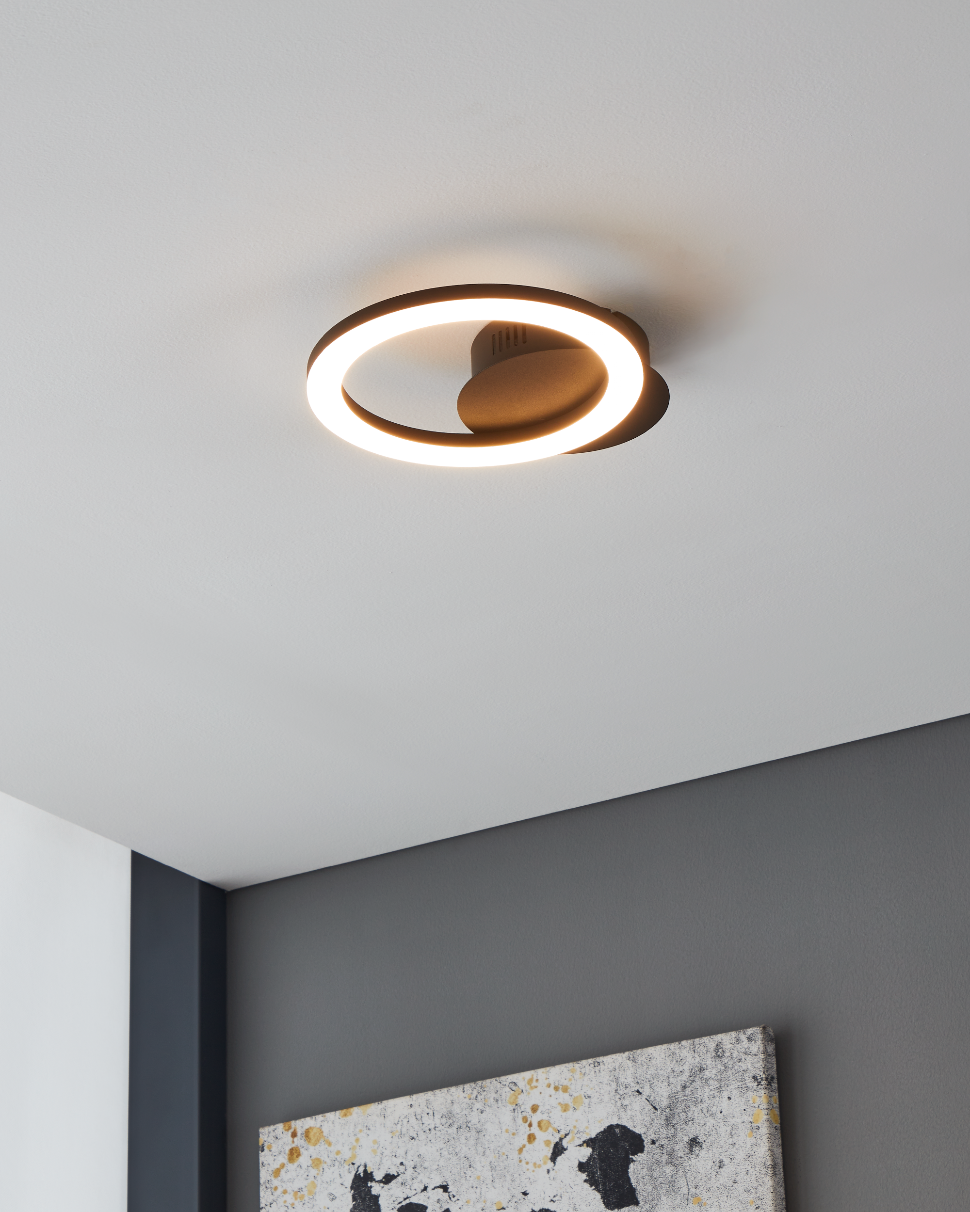 Una moderna plafoniera a forma di anello illumina una stanza con pareti grigie e bianche.
