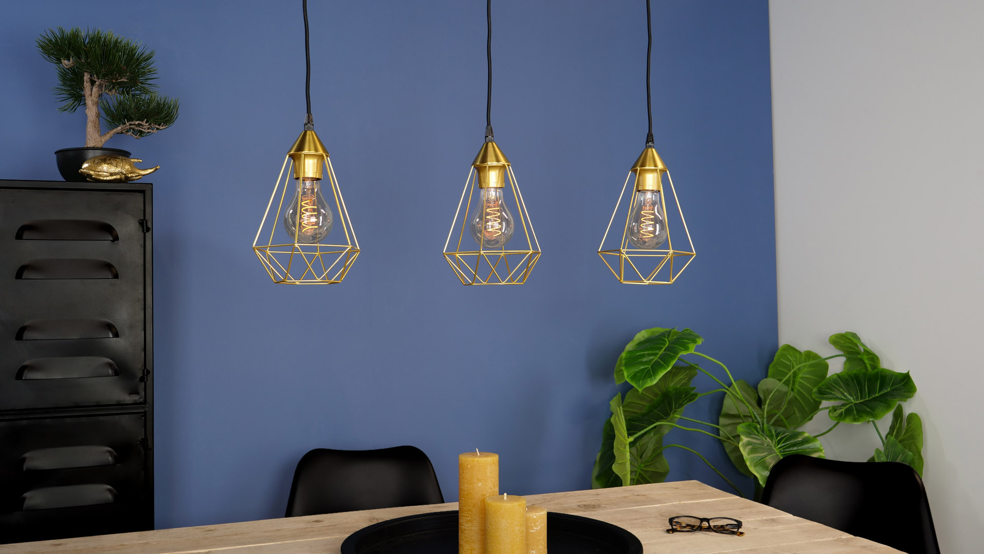 Drei goldene geometrische Pendelleuchten hängen über einem Esstisch in einem modernen Raum.