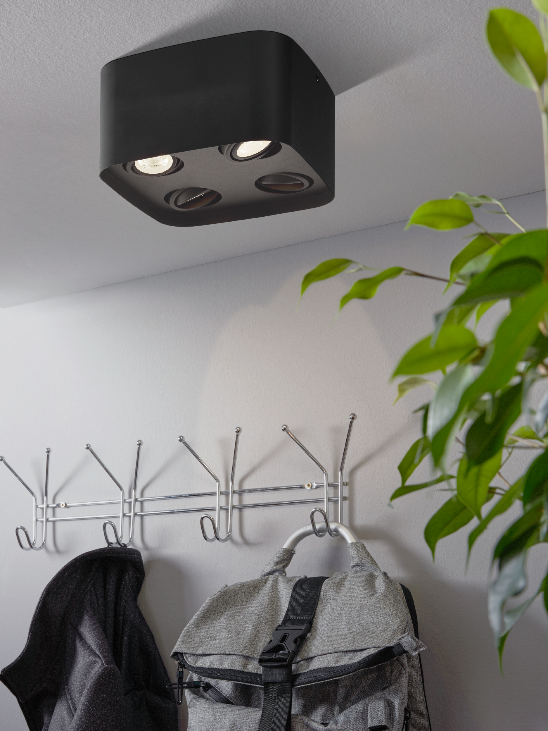Eine schwarze Deckenleuchte über einer Garderobe, an der ein grauer Rucksack und eine dunkle Jacke hängen.