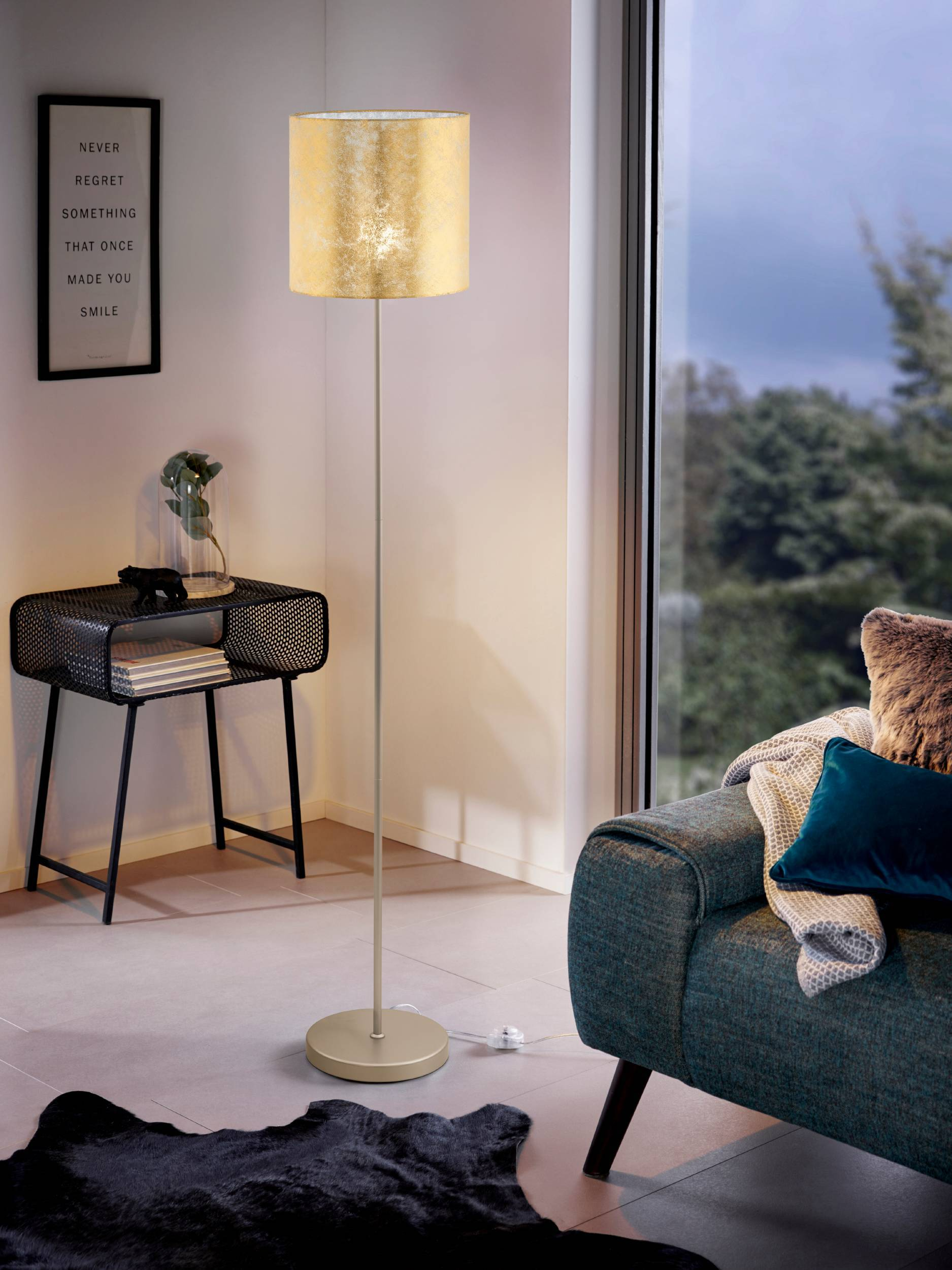 Un lampadaire doré se trouve dans un salon confortable, près d'un canapé et d'une table d'appoint.