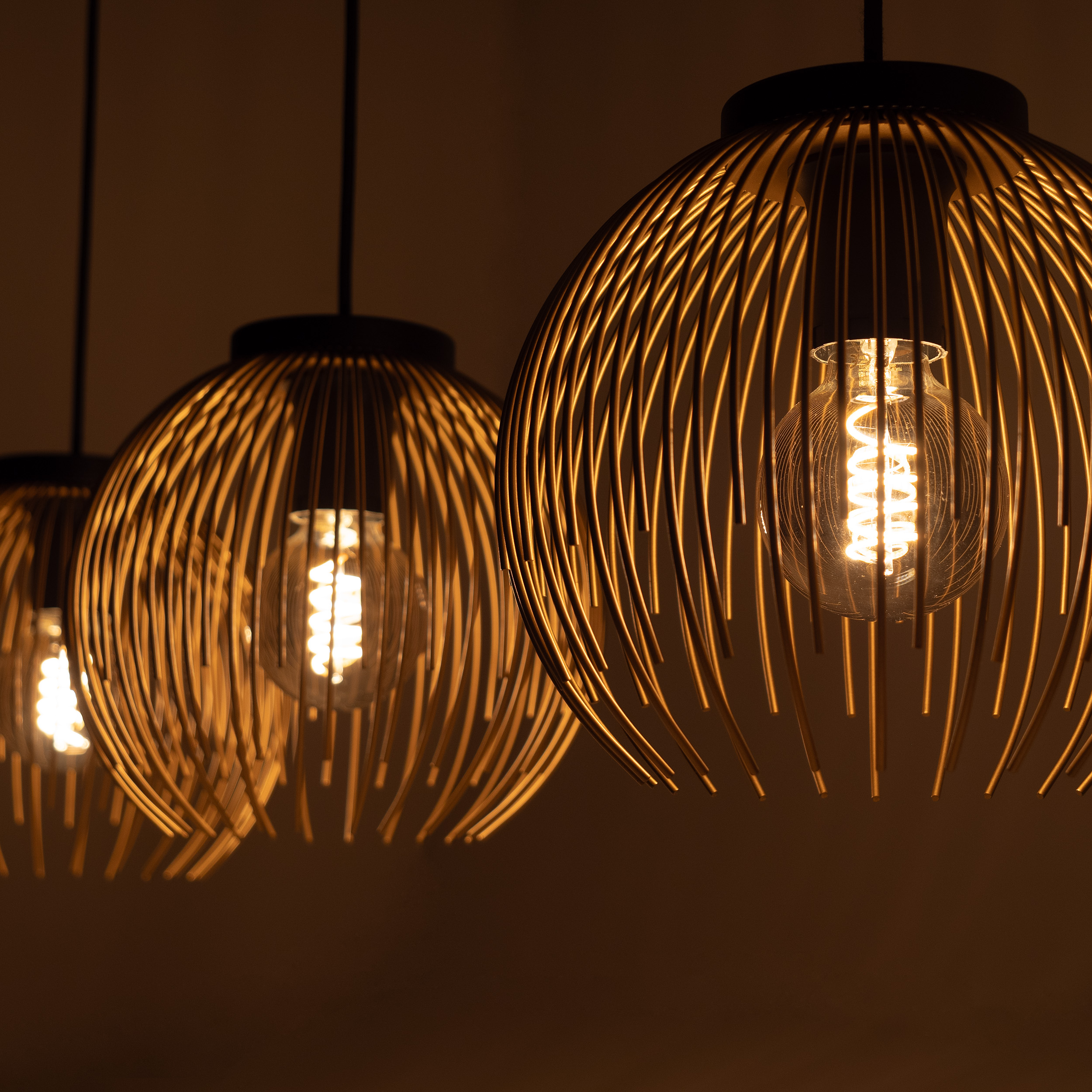 Tre lampade a sospensione in filo dorato con lampadine visibili sono mostrate da vicino.