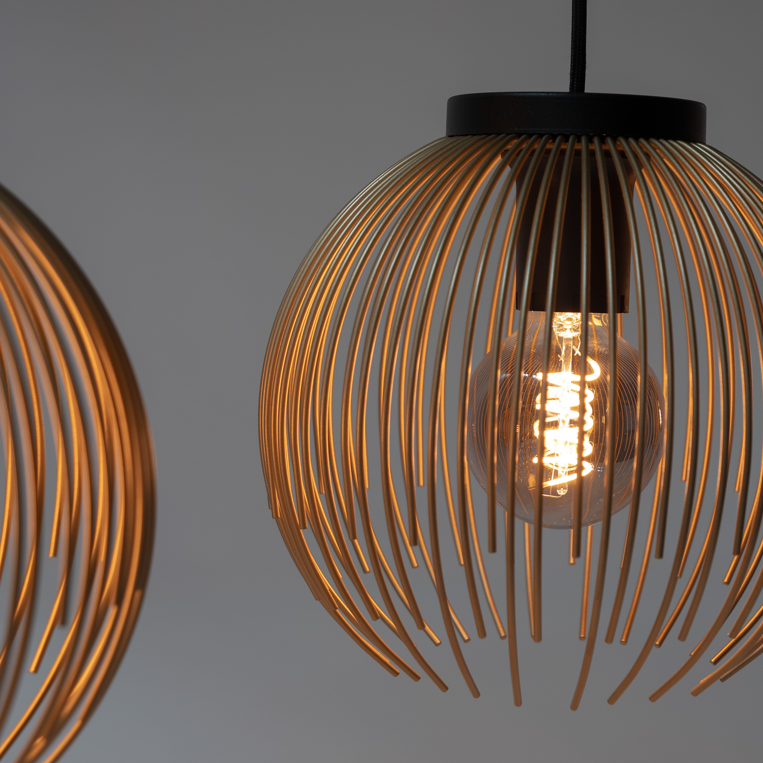 Un primo piano mostra una lampada a sospensione in filo dorato con una lampadina visibile.