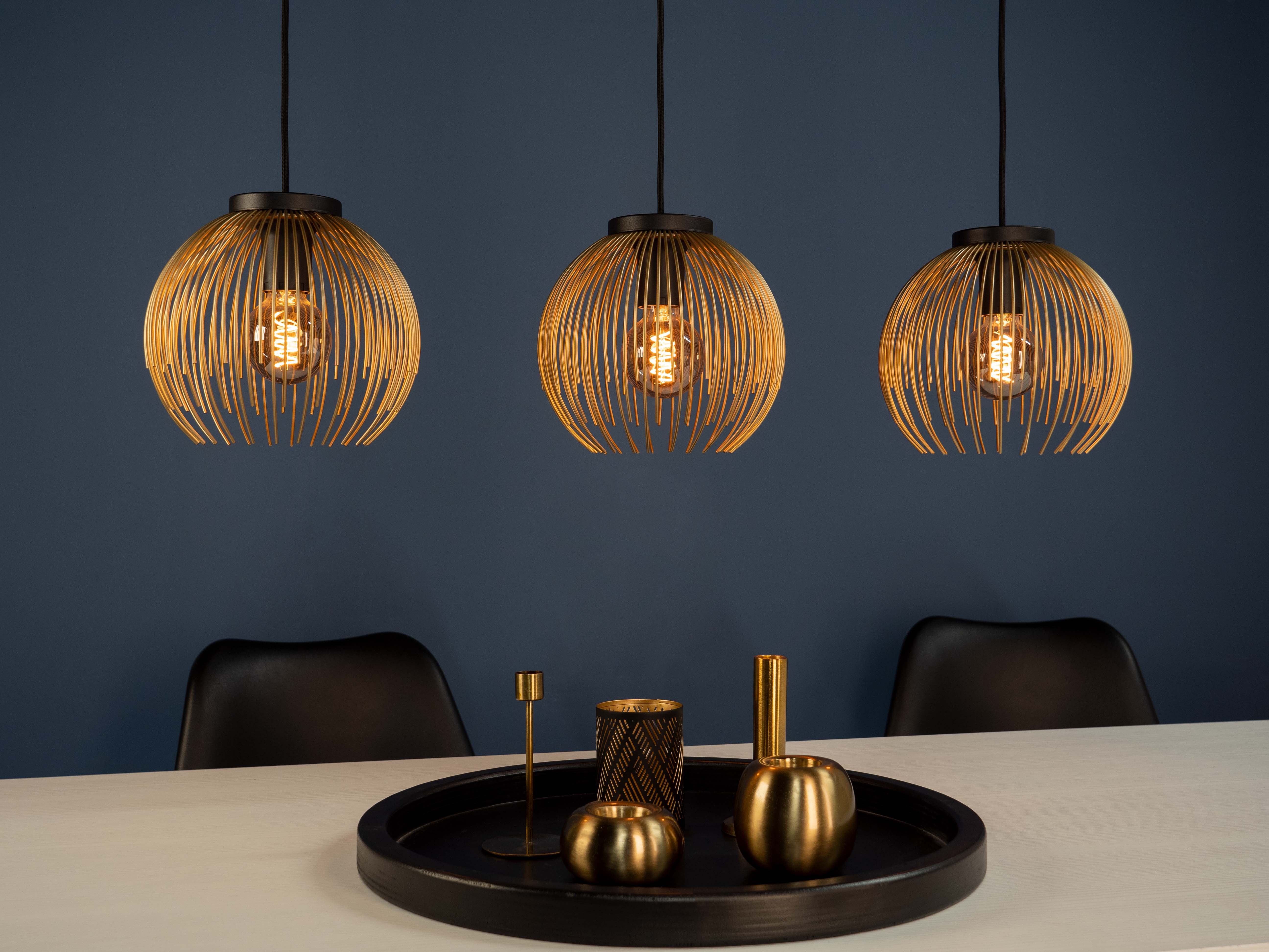 Tre lampade a sospensione in filo dorato pendono sopra un tavolo con oggetti decorativi.