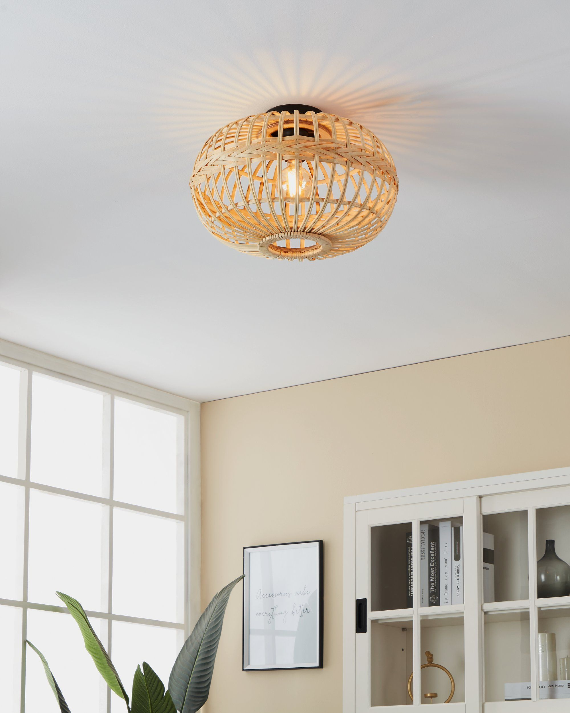 Lampada da soffitto in bambù intrecciato in una stanza con soffitto e pareti bianche, un quadro e un armadio.