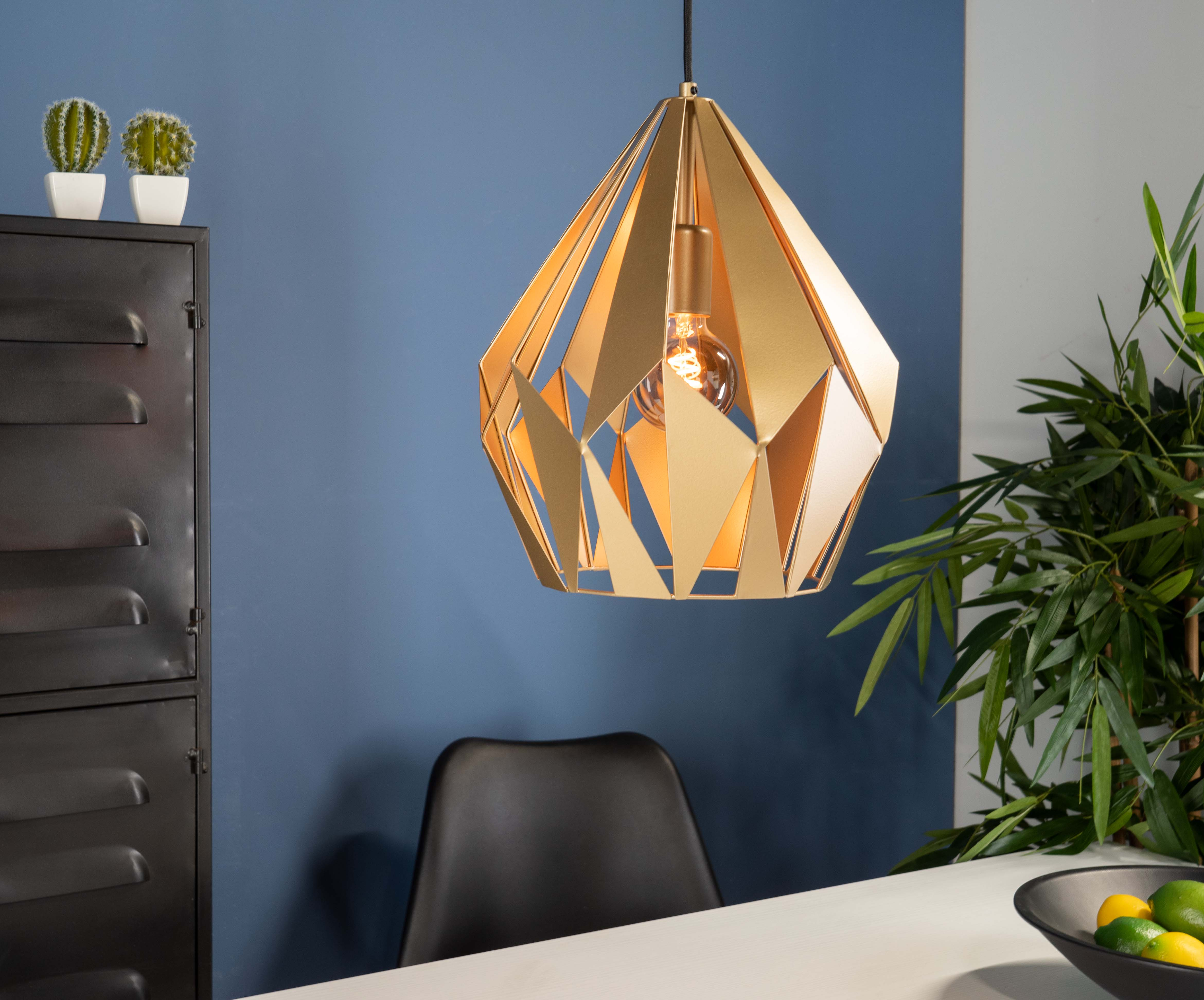 Eine goldene geometrische Pendelleuchte hängt in einem Raum mit einer Pflanze und Möbeln.