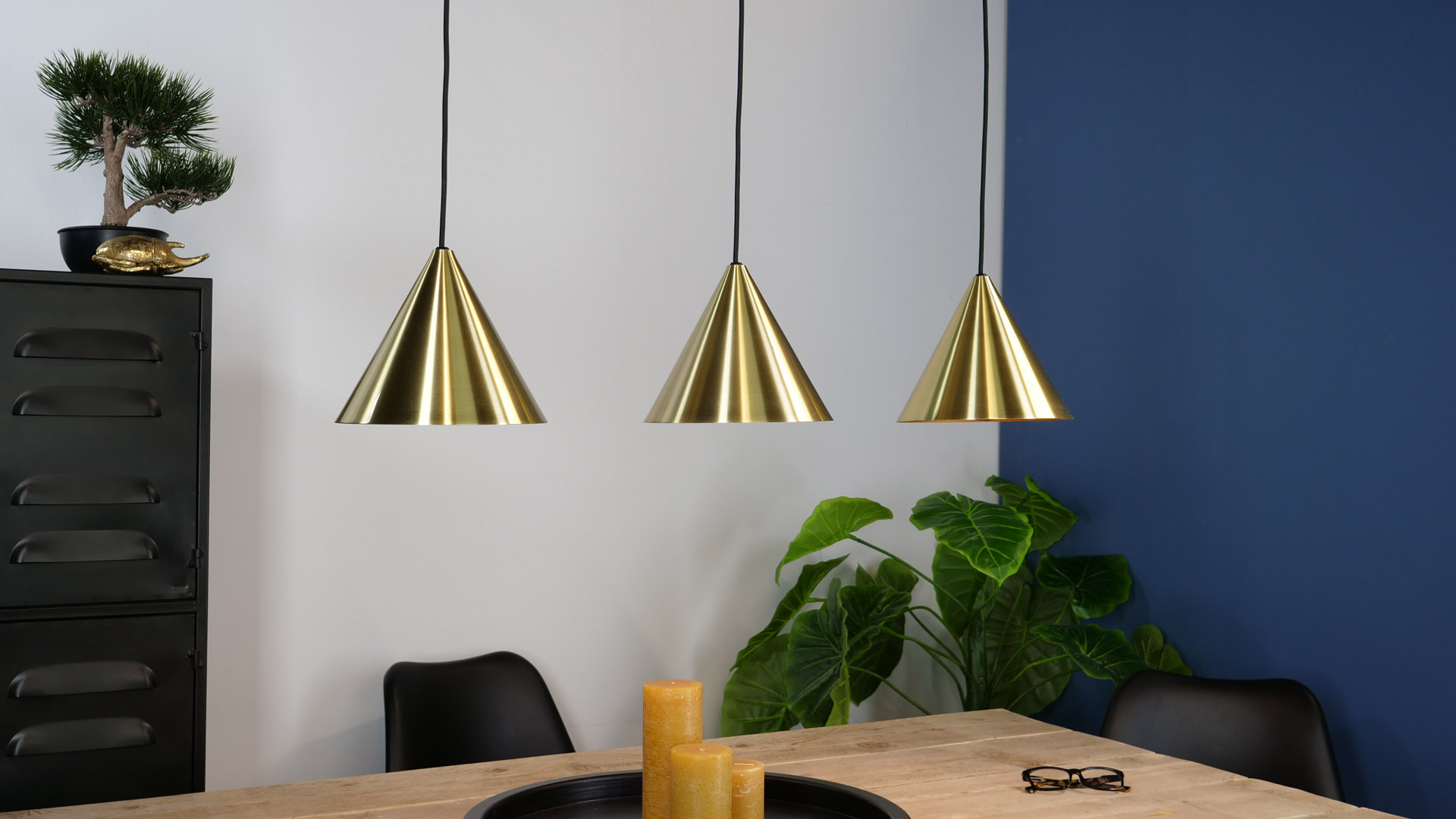 Drei goldene Pendelleuchten hängen über einem Holztisch mit Stühlen und Dekoration.