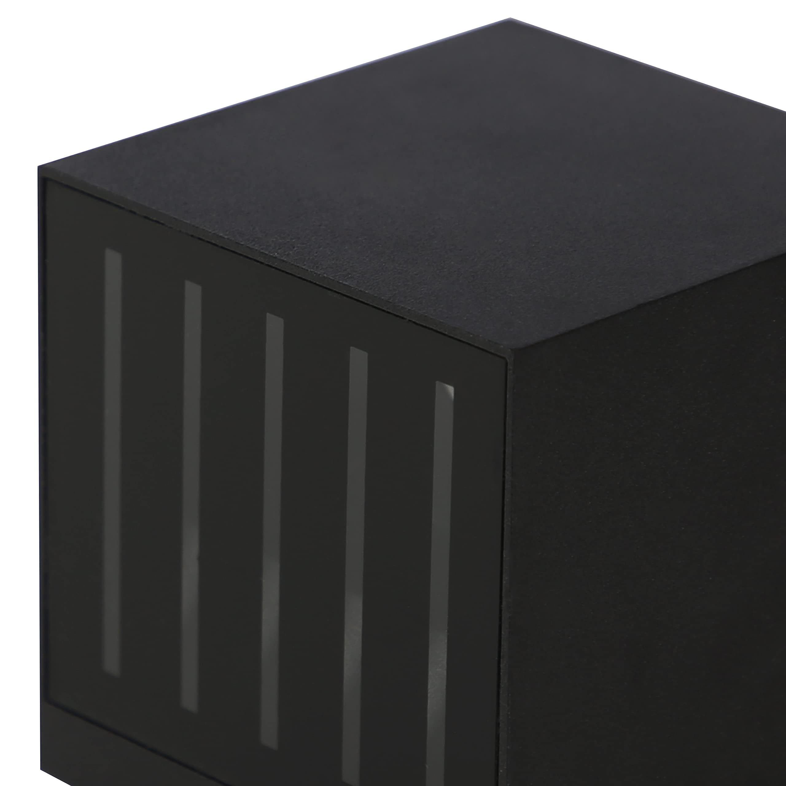 Un primo piano di una lampada da parete nera a forma di cubo mostra la sua superficie ruvida e le fessure di luce verticali sul lato.