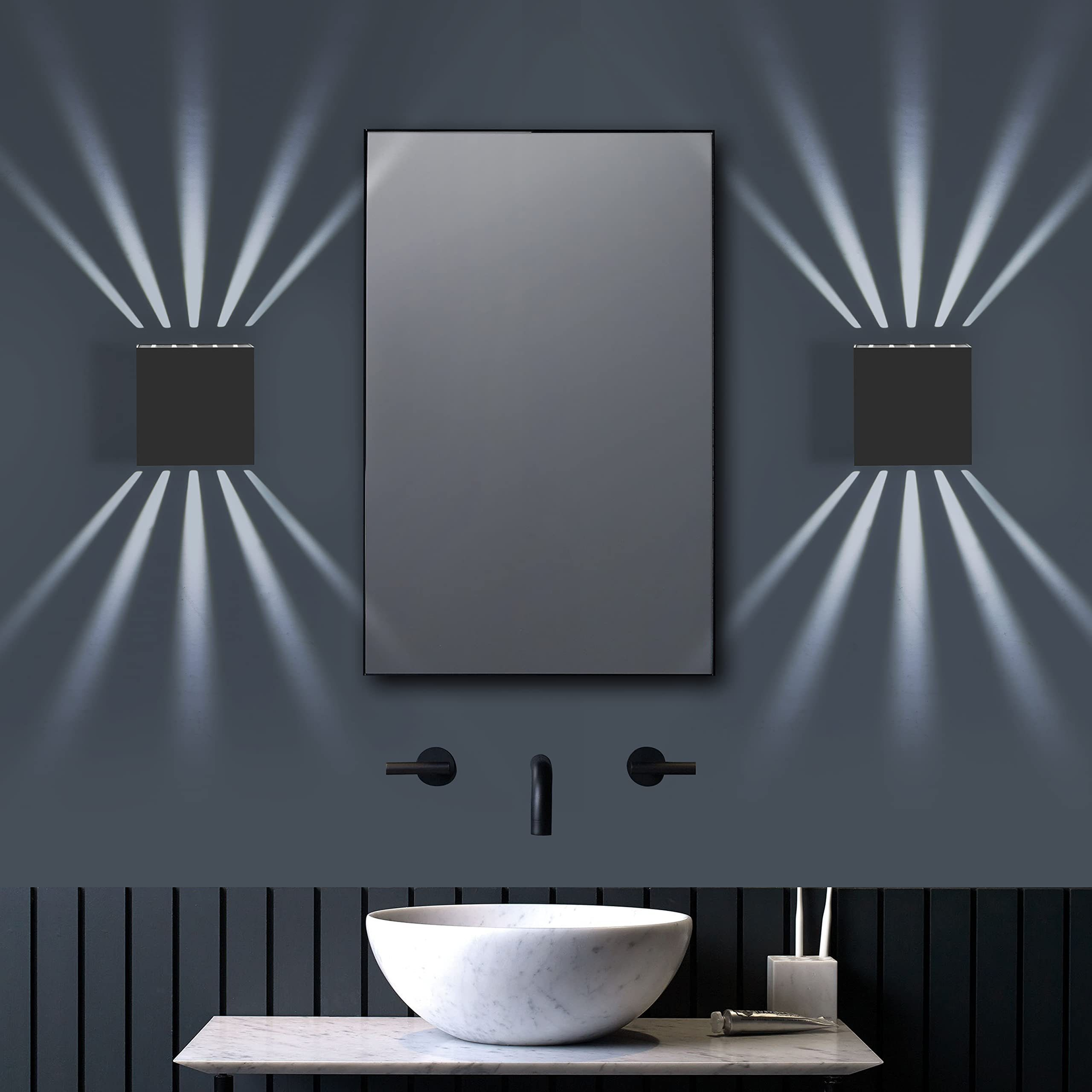 Un bagno presenta due lampade da parete a forma di cubo che fiancheggiano uno specchio sopra un lavandino con un piano in marmo.