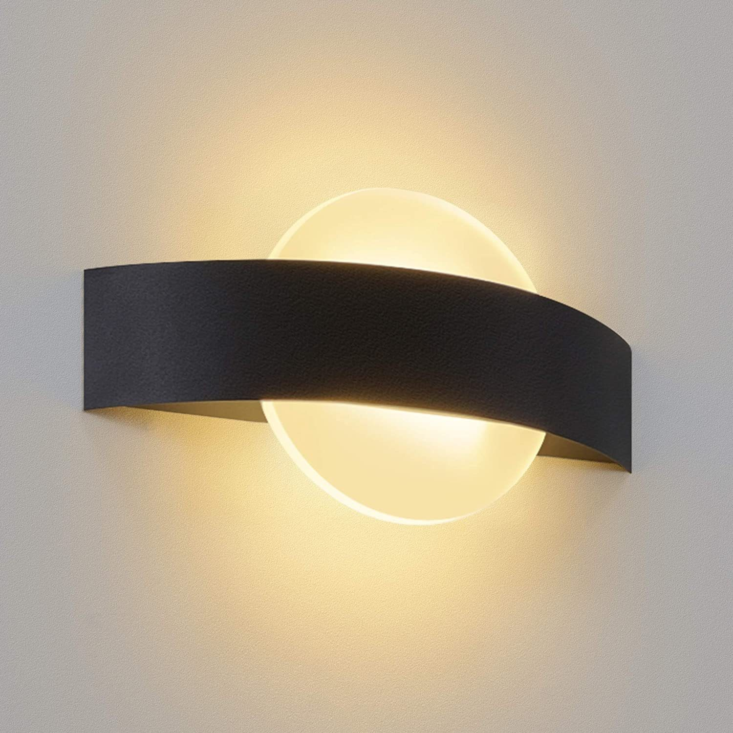 Una moderna lampada da parete con una fascia curva nera sopra un disco bianco, montata su una parete grigio chiaro.