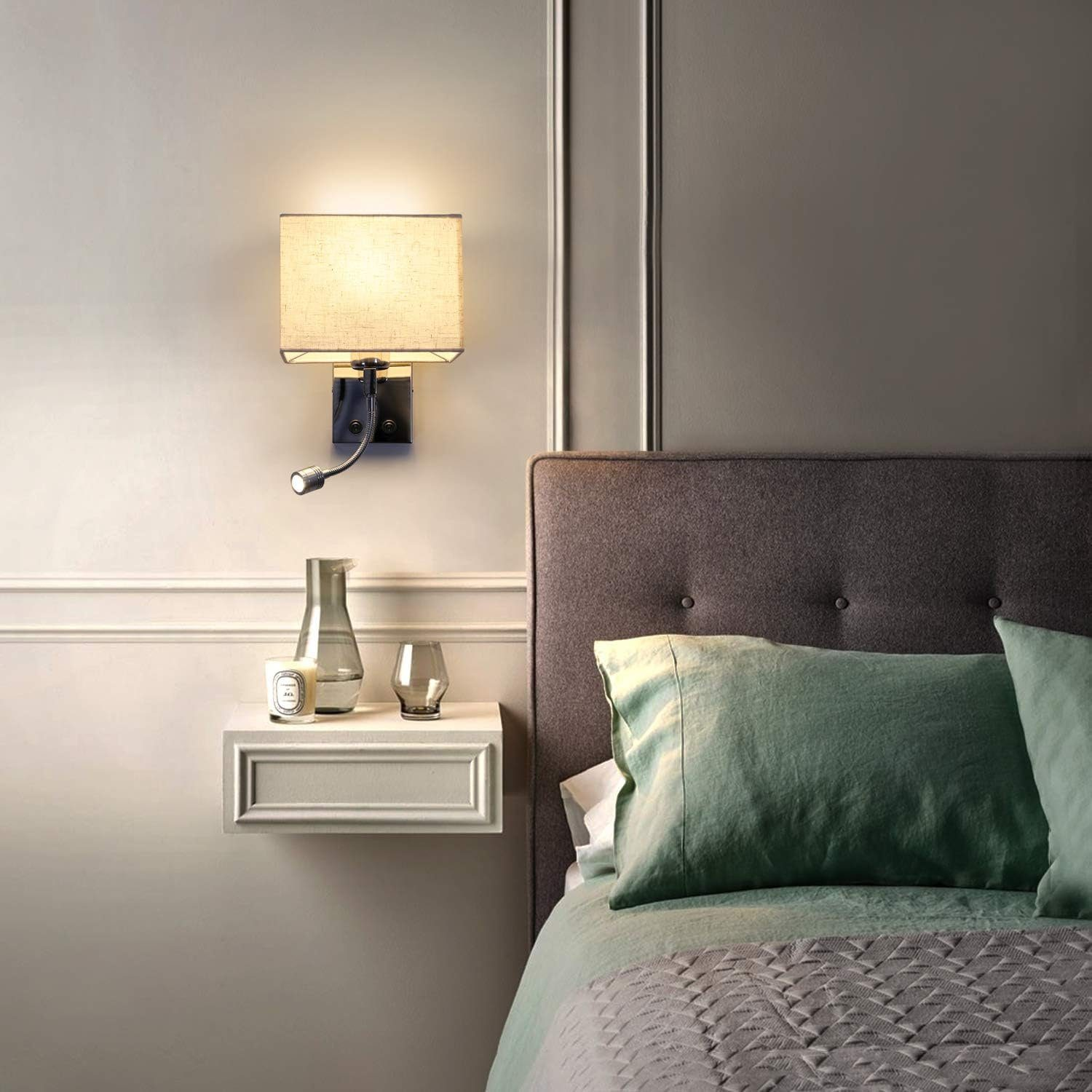 Una scena di camera da letto con una lampada da parete, un comodino e un letto con cuscini verdi e coperta grigia.