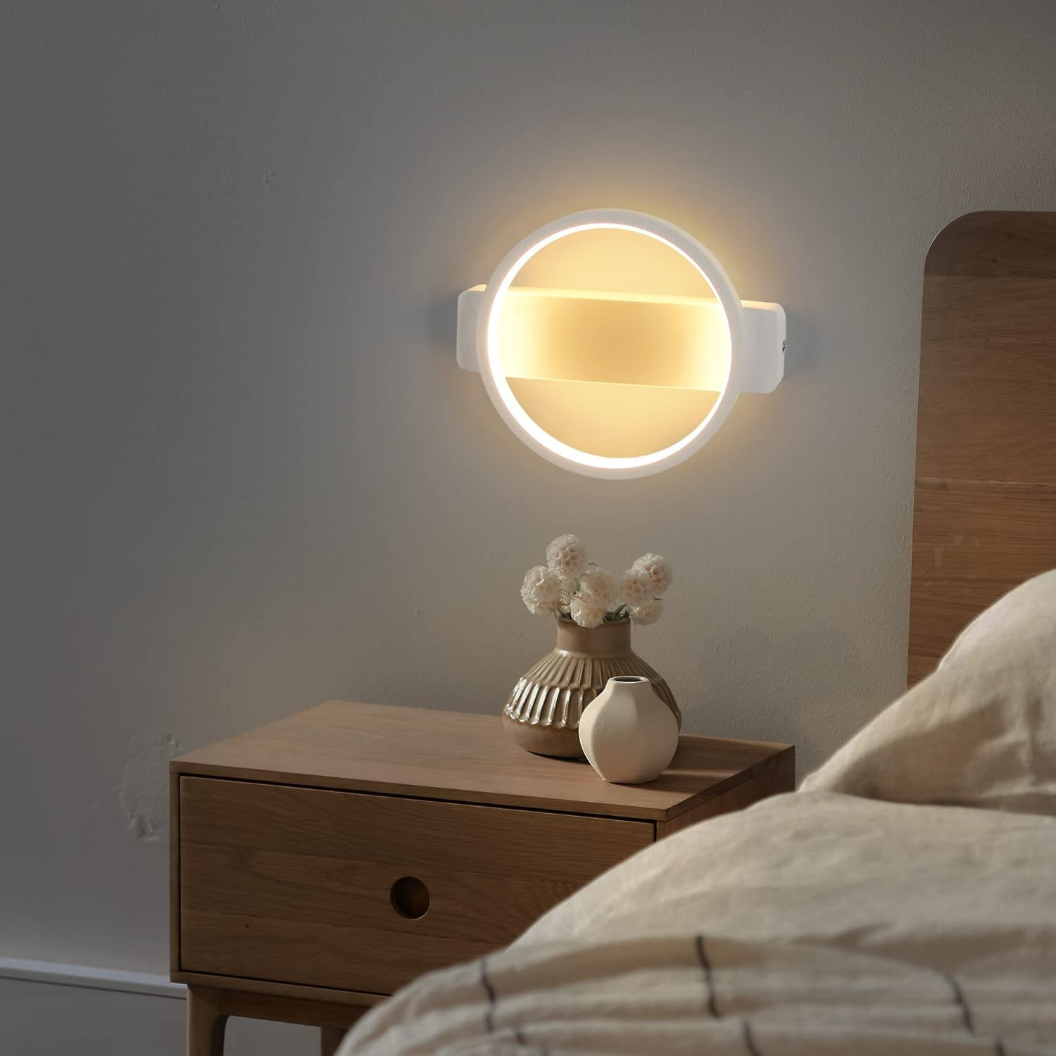 Stolik nocny z lampą. Lampa jest okrągła i emituje ciepłe światło. Obok stoi wazon z kwiatami.