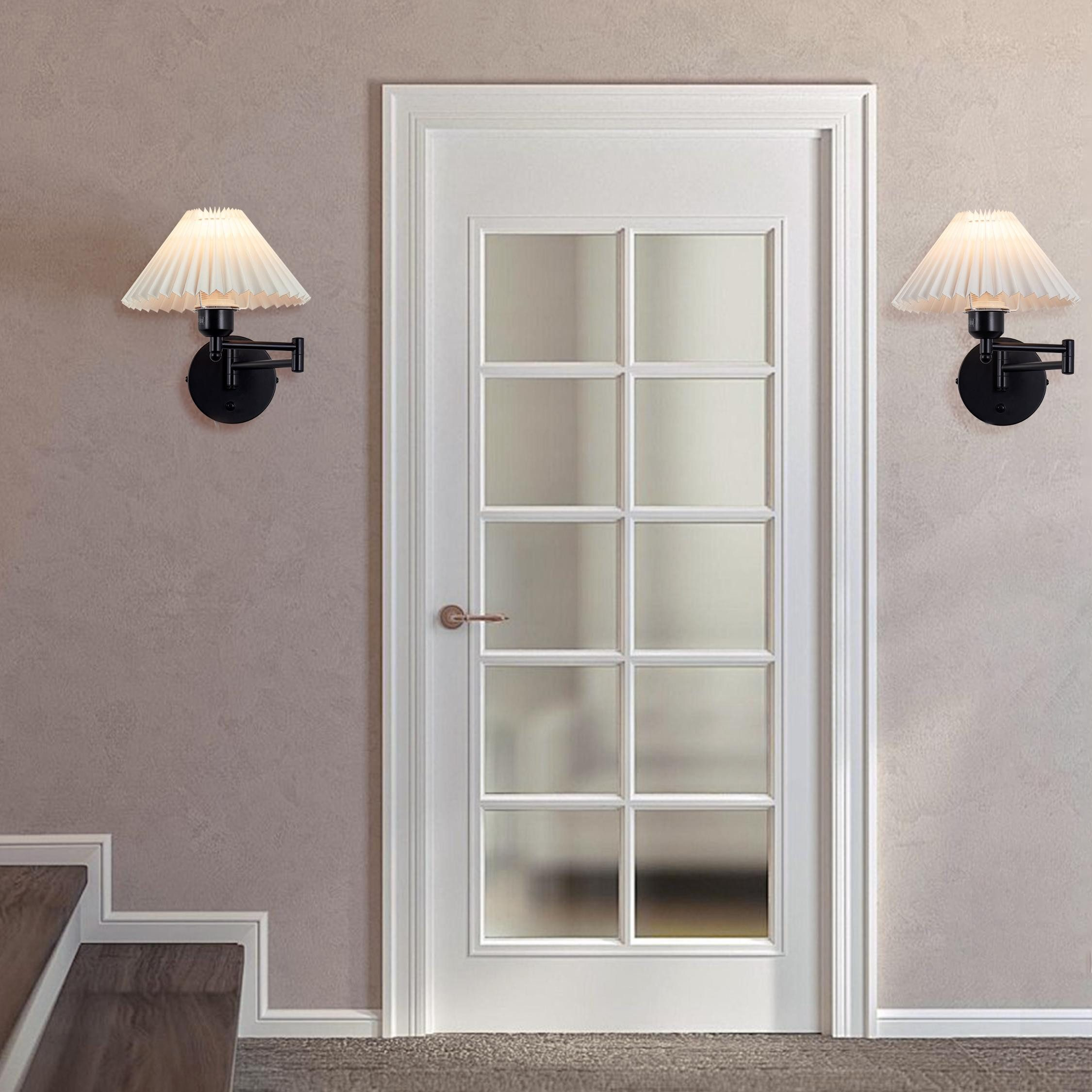 Due applique fiancheggiano una porta bianca a pannelli con inserti in vetro, su una parete viola chiaro e una scala.