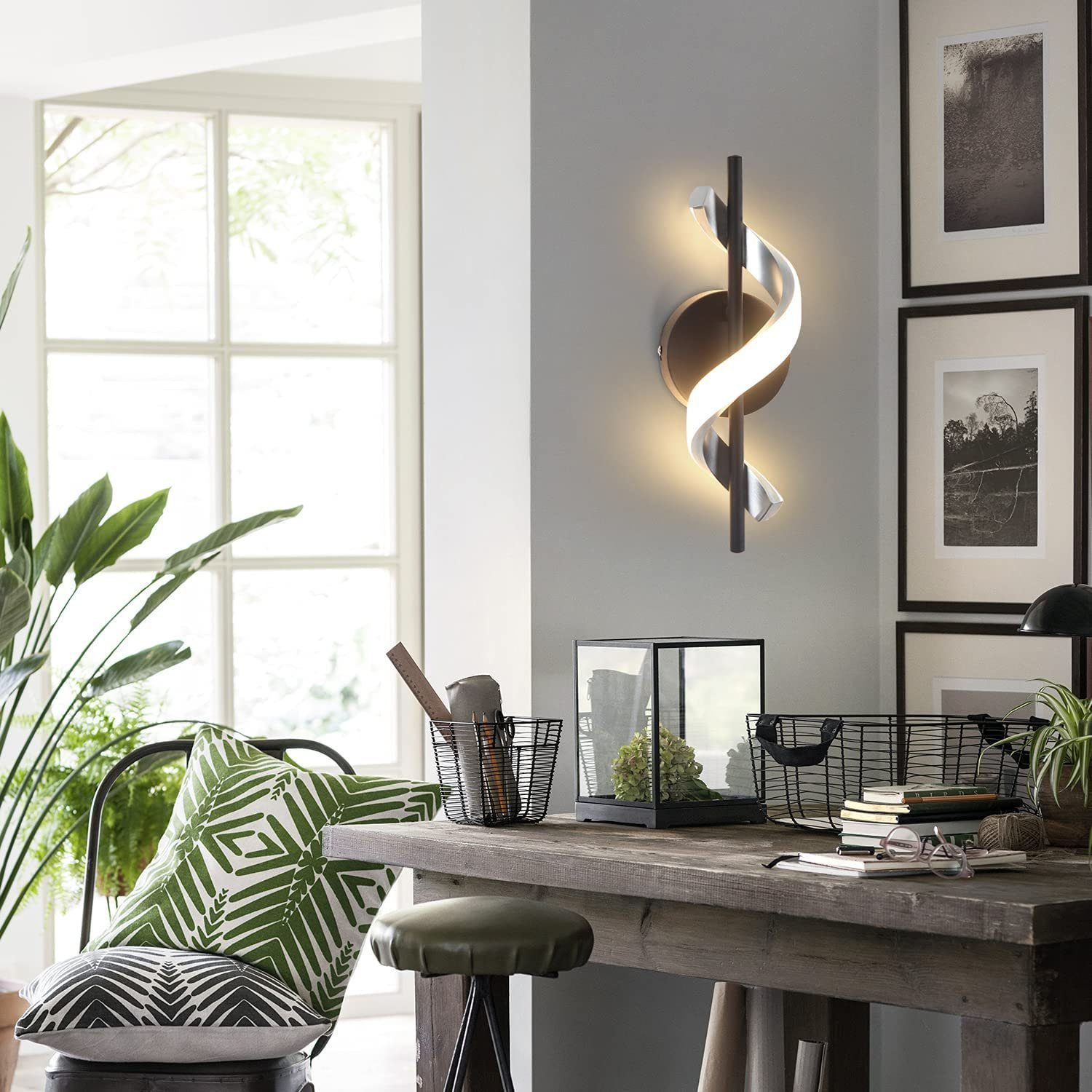 Una lampada da parete moderna con design curvo, una scrivania in legno, una finestra e un cuscino verde con motivo bianco.