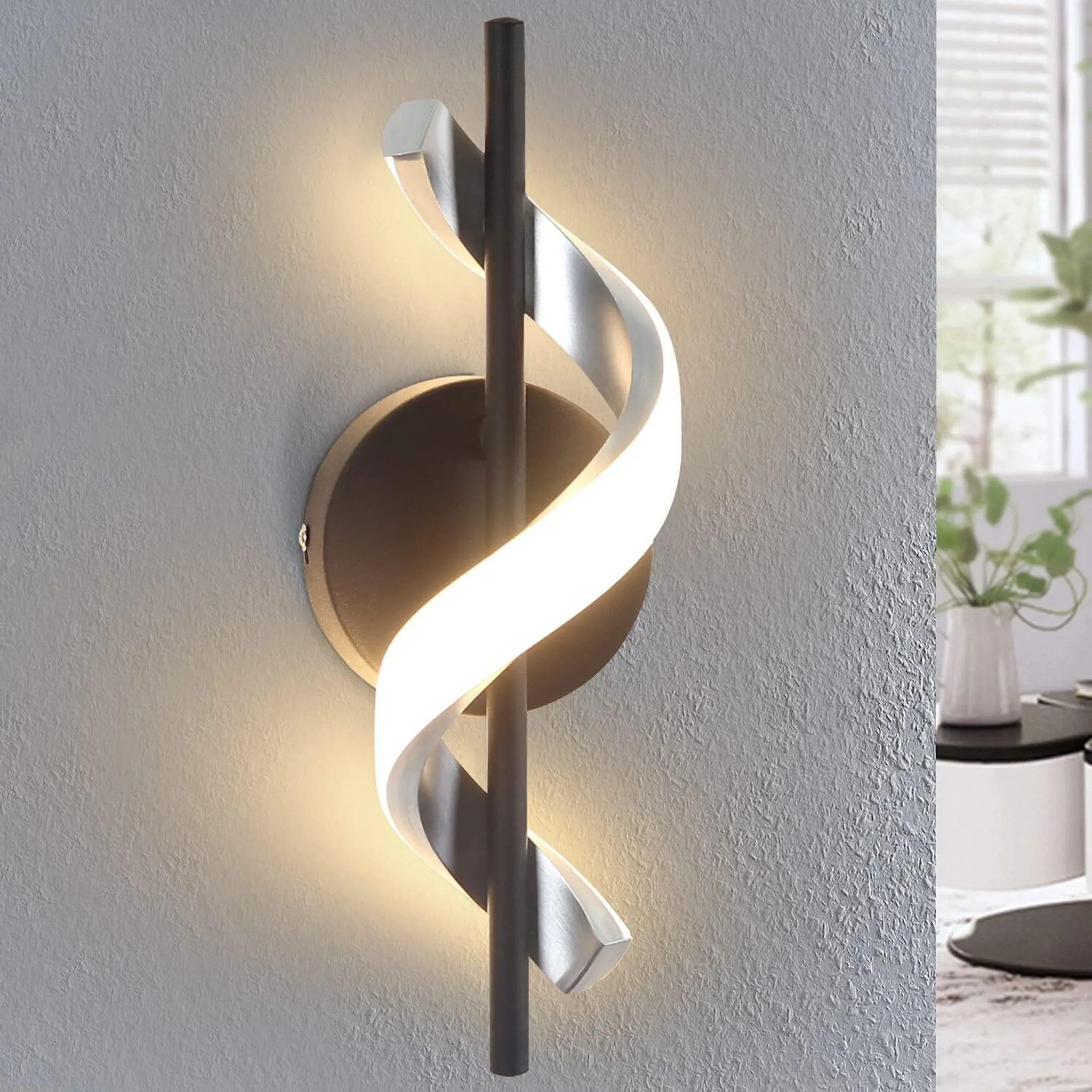 Lampada da parete moderna con design curvo, elementi neri, argentati, luce intensa su parete grigio chiaro.