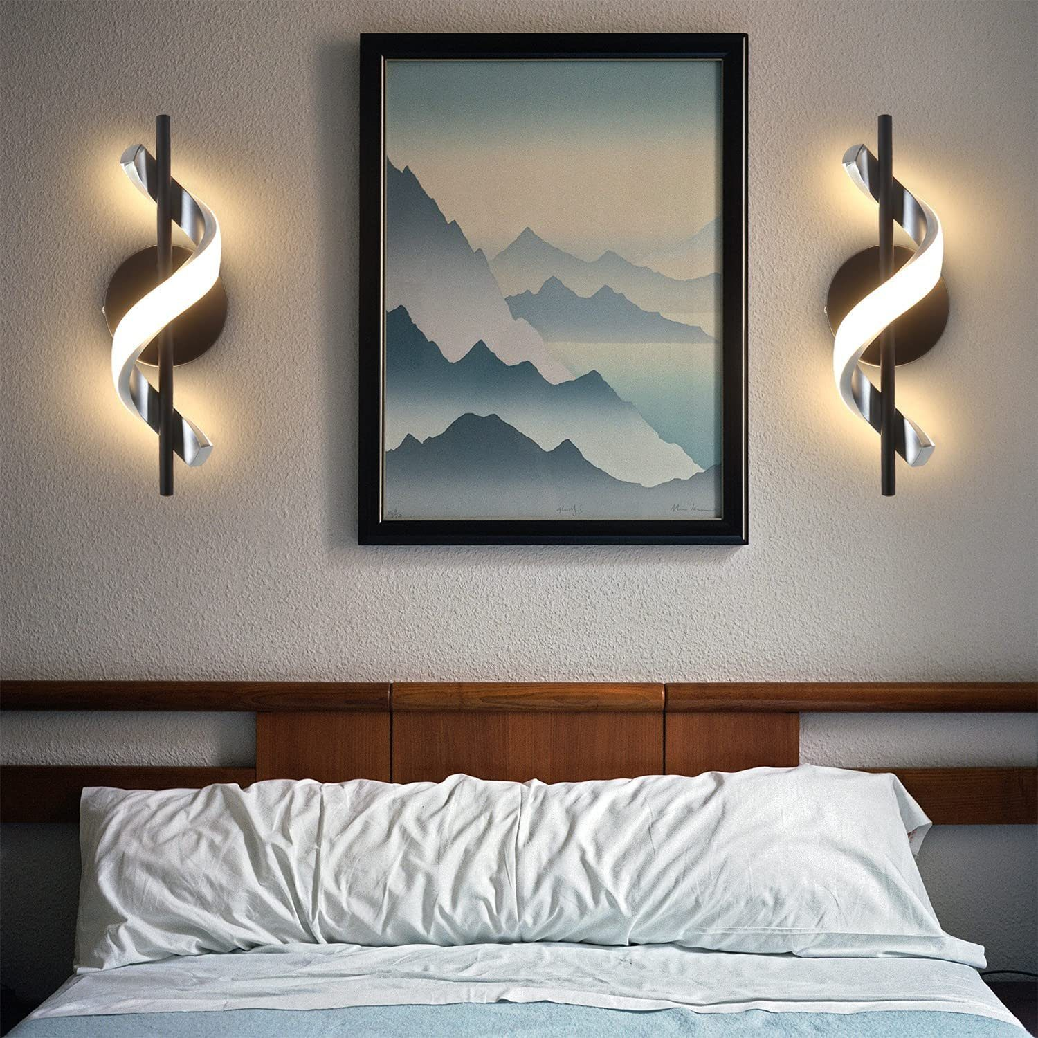 Due lampade da parete con design curvo, montate su un muro con un dipinto sopra un letto. Le lampade sono luminose.