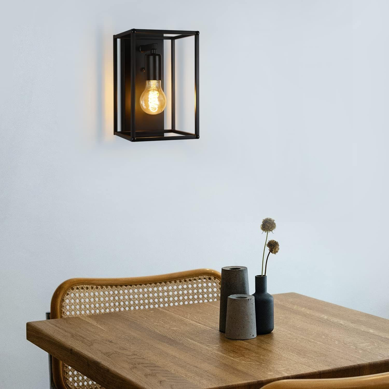 Jadalnia z czarną oprawioną lampą ścienną, drewnianym stołem i plecionymi krzesłami.