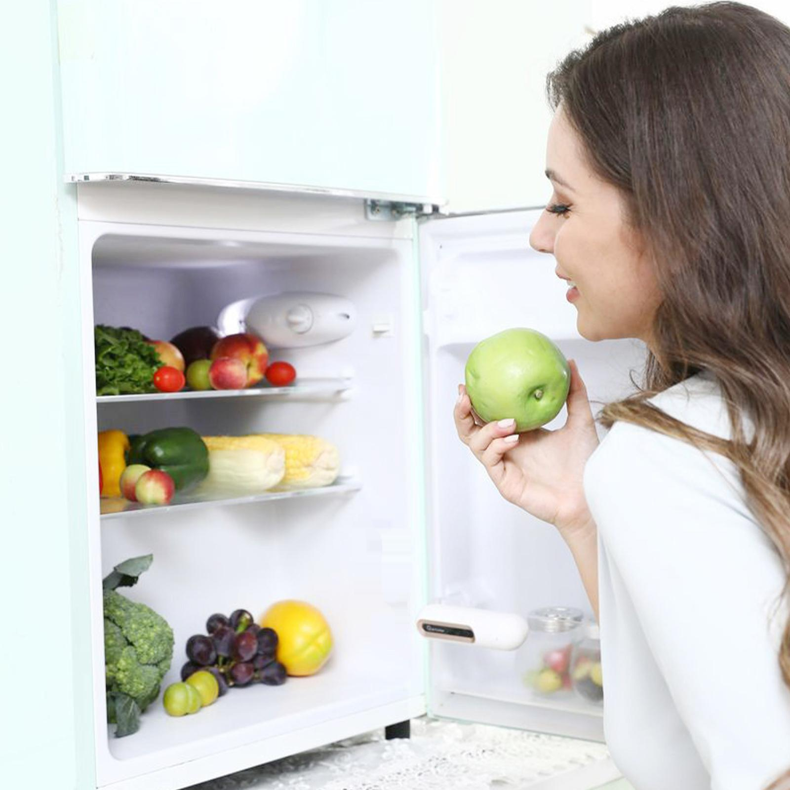 Eine Frau betrachtet einen grünen Apfel. Ein Kühlschrank mit Gemüse und Obst ist geöffnet.