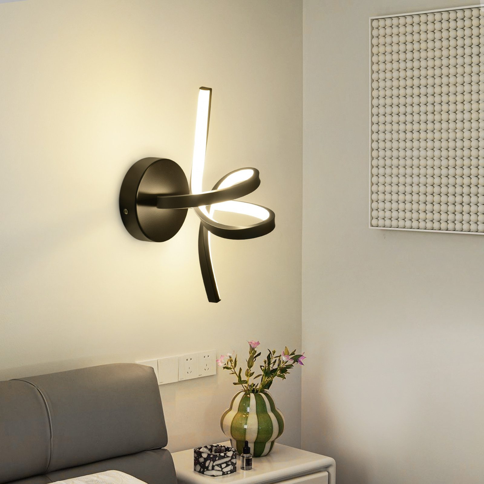 Applique moderna su parete beige vicino a un comodino con decorazioni, fiori e prese di corrente.