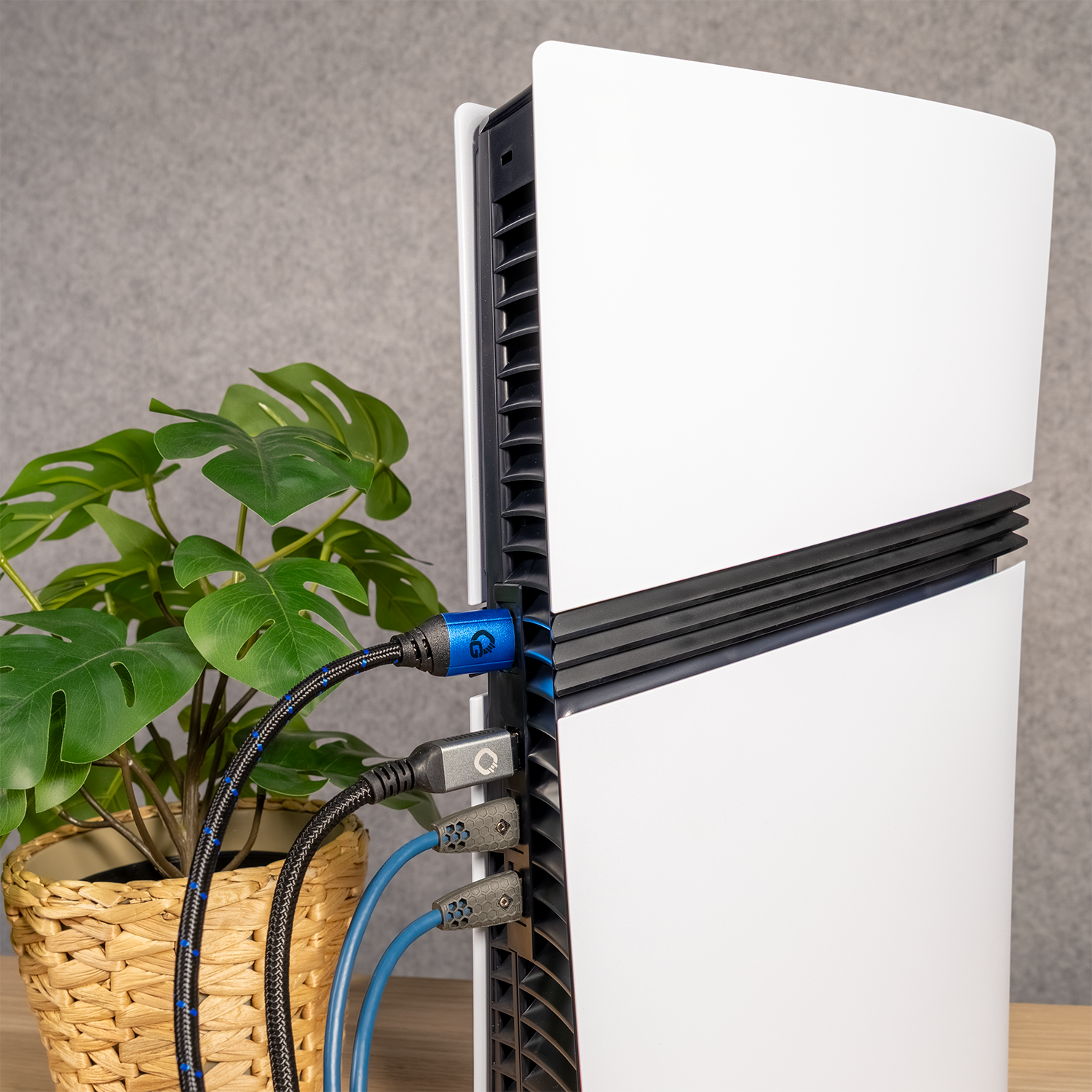 Eine weiße PlayStation 5-Konsole mit mehreren angeschlossenen Kabeln, neben einer Pflanze in einem Weidenkorb.