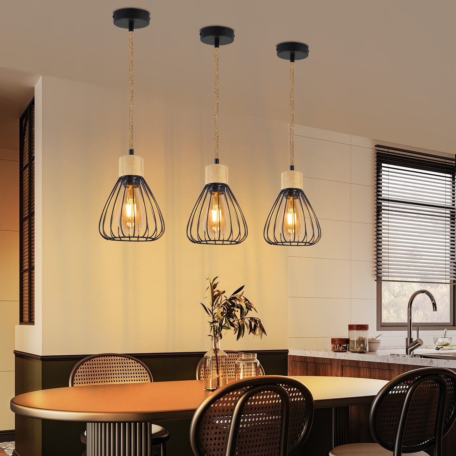 Trzy lampy wiszące z czarnymi kloszami z drutu wiszą nad jadalnią ze stołem, krzesłami i kuchnią w tle.