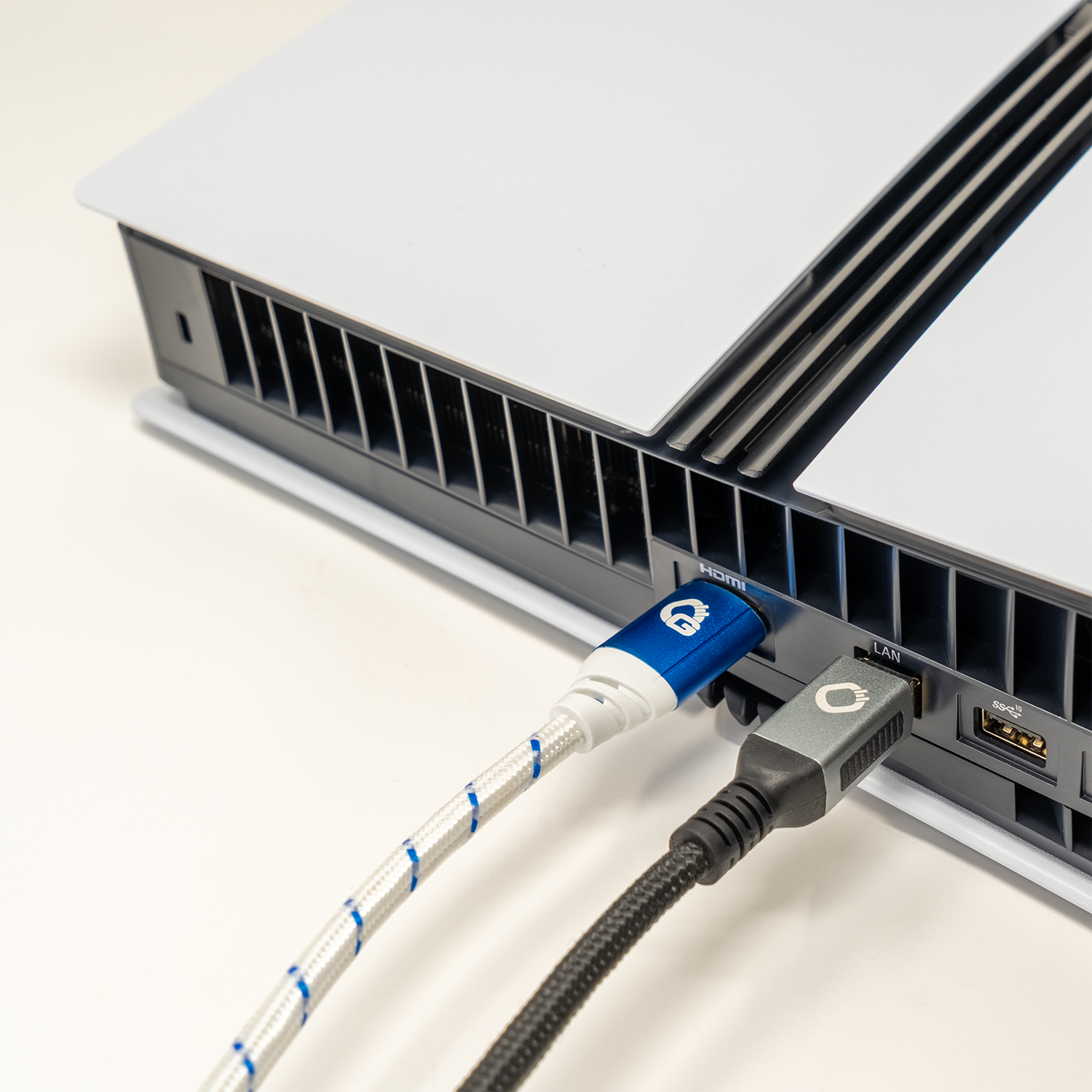 Eine weiße Spielekonsole mit einem blau-weißen HDMI-Kabel, das neben einem schwarzen Kabel eingesteckt ist, auf einer weißen Oberfläche.