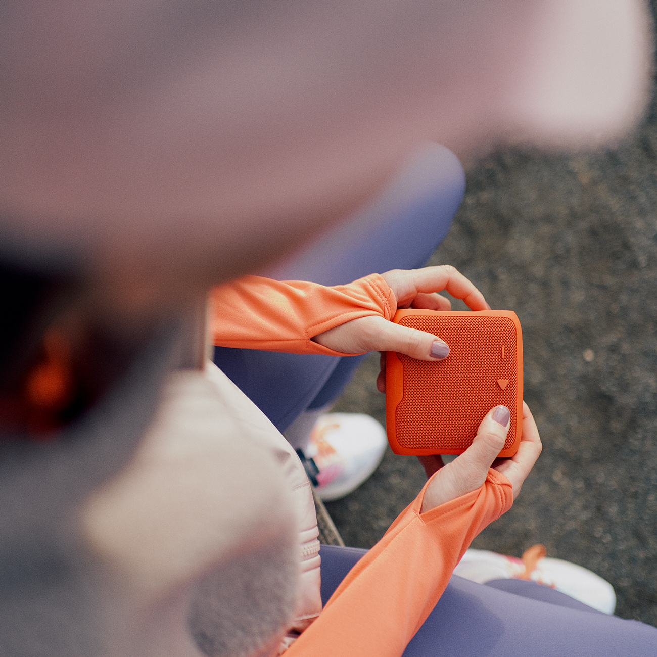 Persoon die een oranje luidspreker vasthoudt, close-up. Ze dragen oranje en paarse sportkleding.