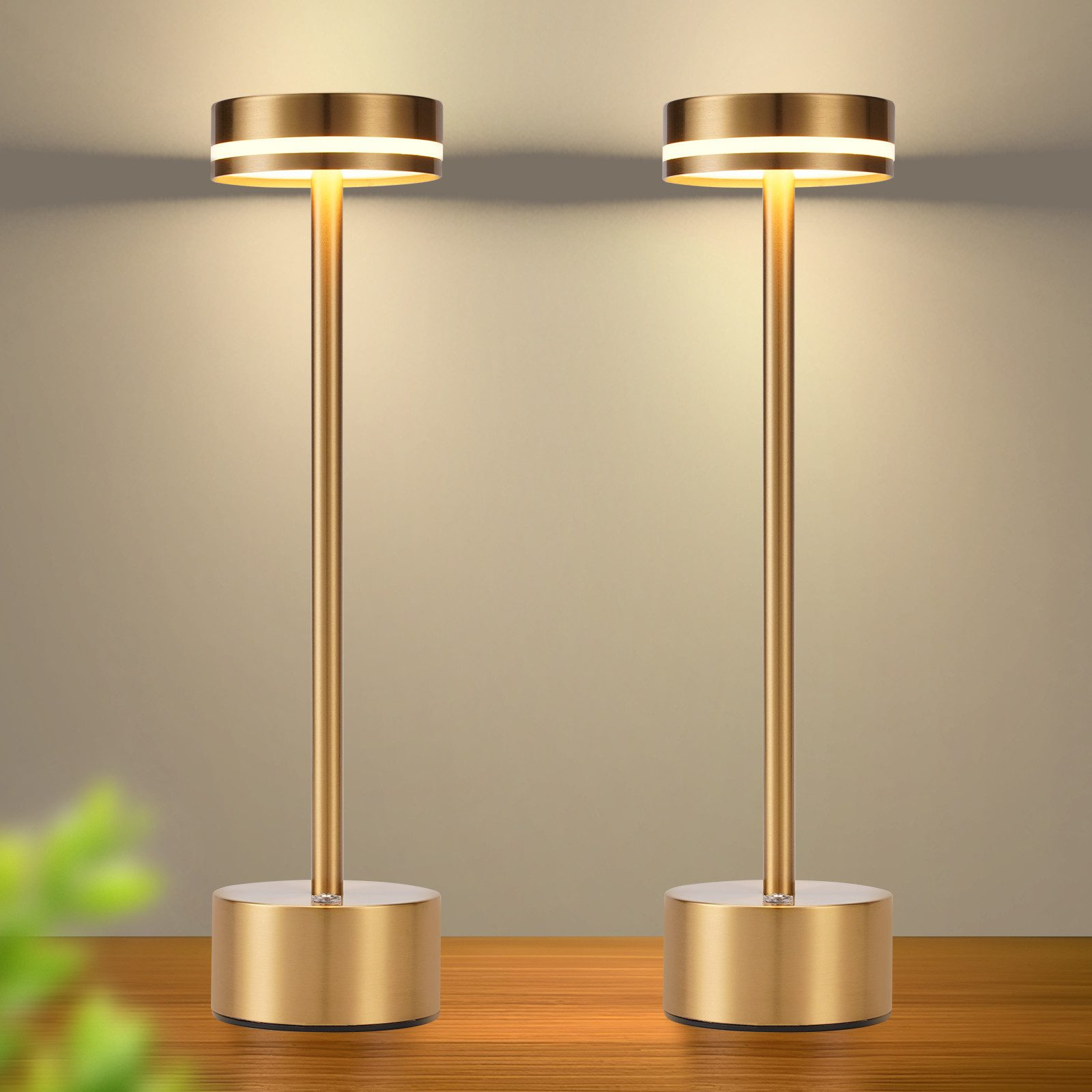 Dwie złote lampy stołowe oświetlają drewnianą powierzchnię na neutralnym tle, tworząc ciepłą poświatę.