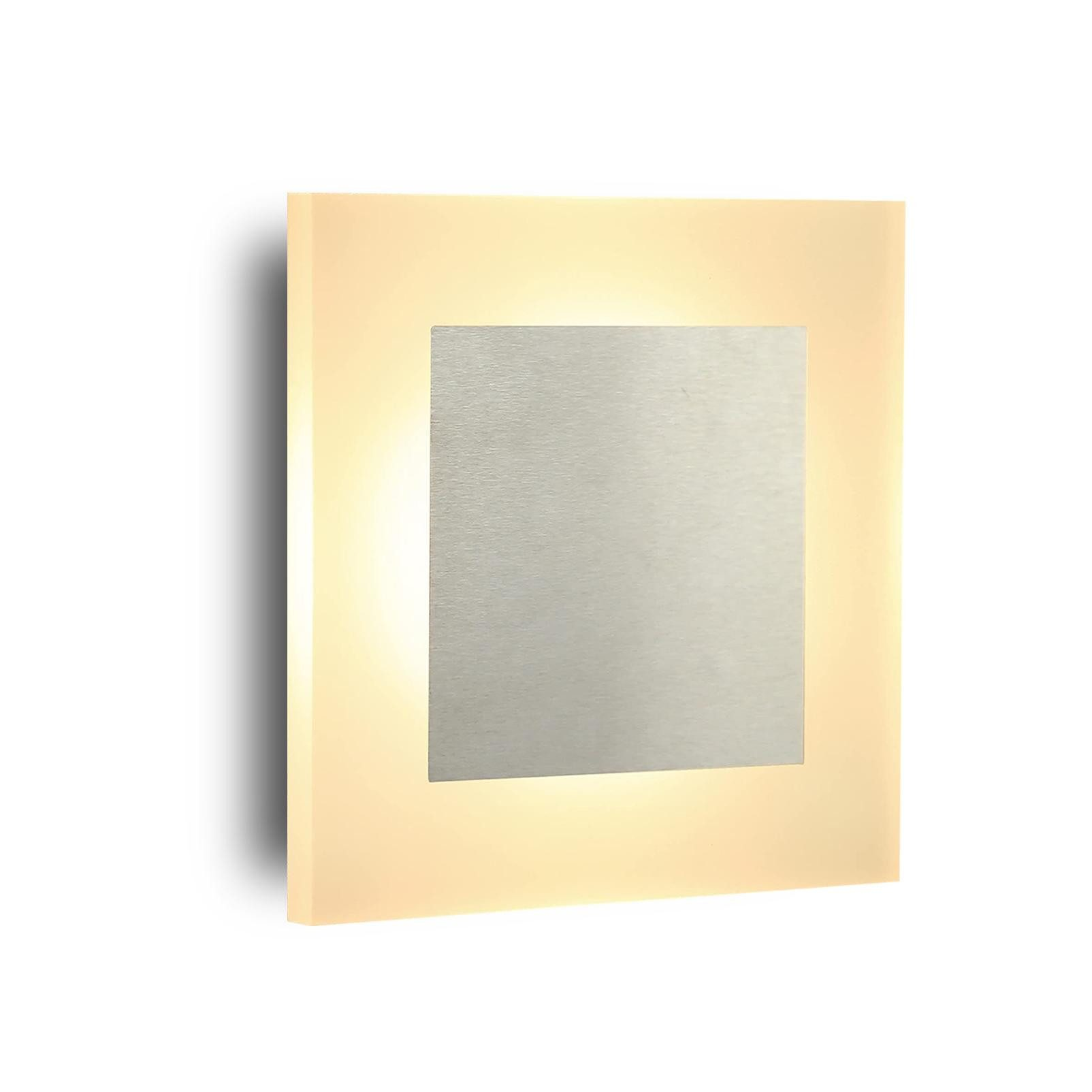 Una luce da parete quadrata con un centro argentato è illuminata su uno sfondo bianco.