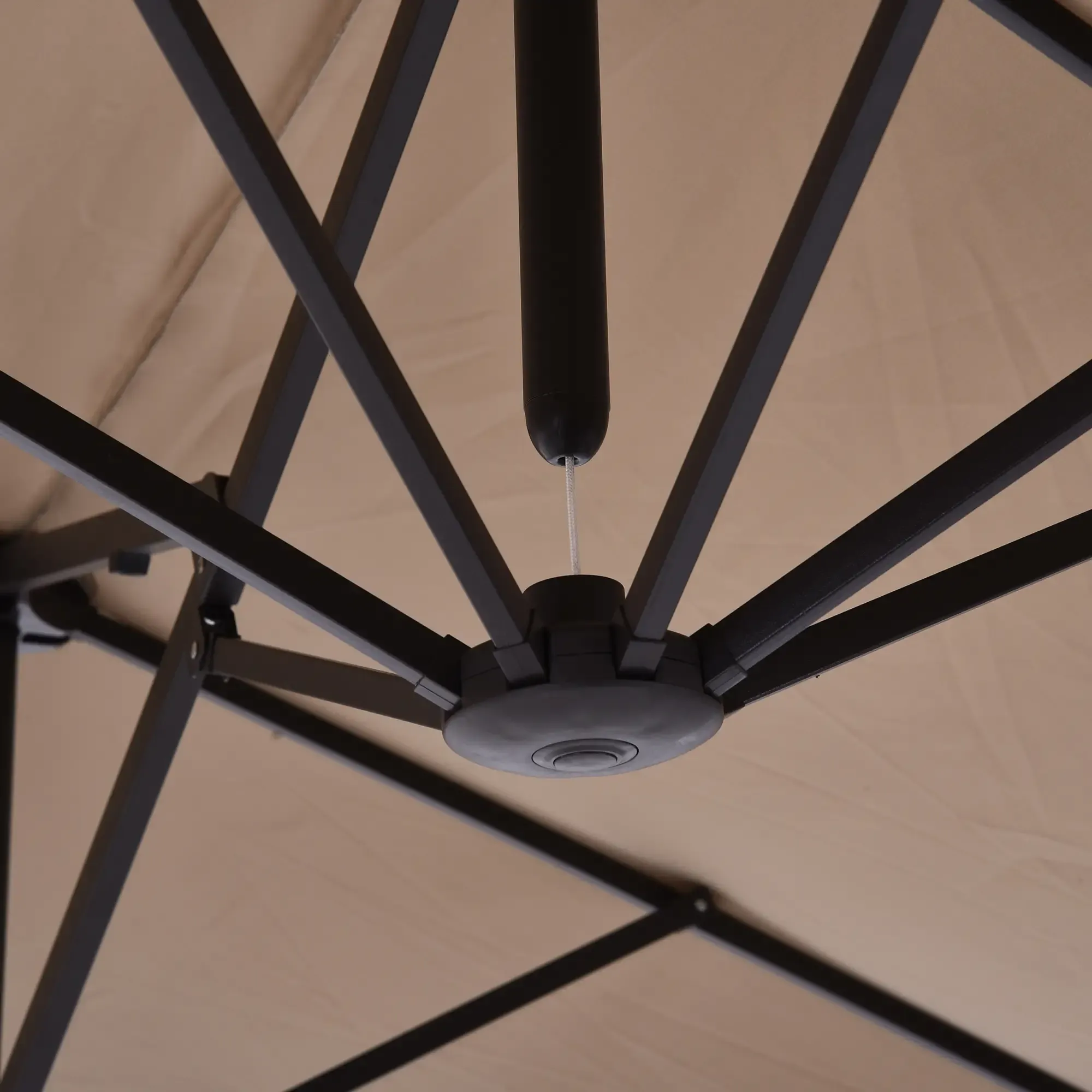 Eine Nahaufnahme zeigt die Unterseite eines beigen Terrassenschirms mit einem schwarzen Metallgestell vor einem beigen Hintergrund.