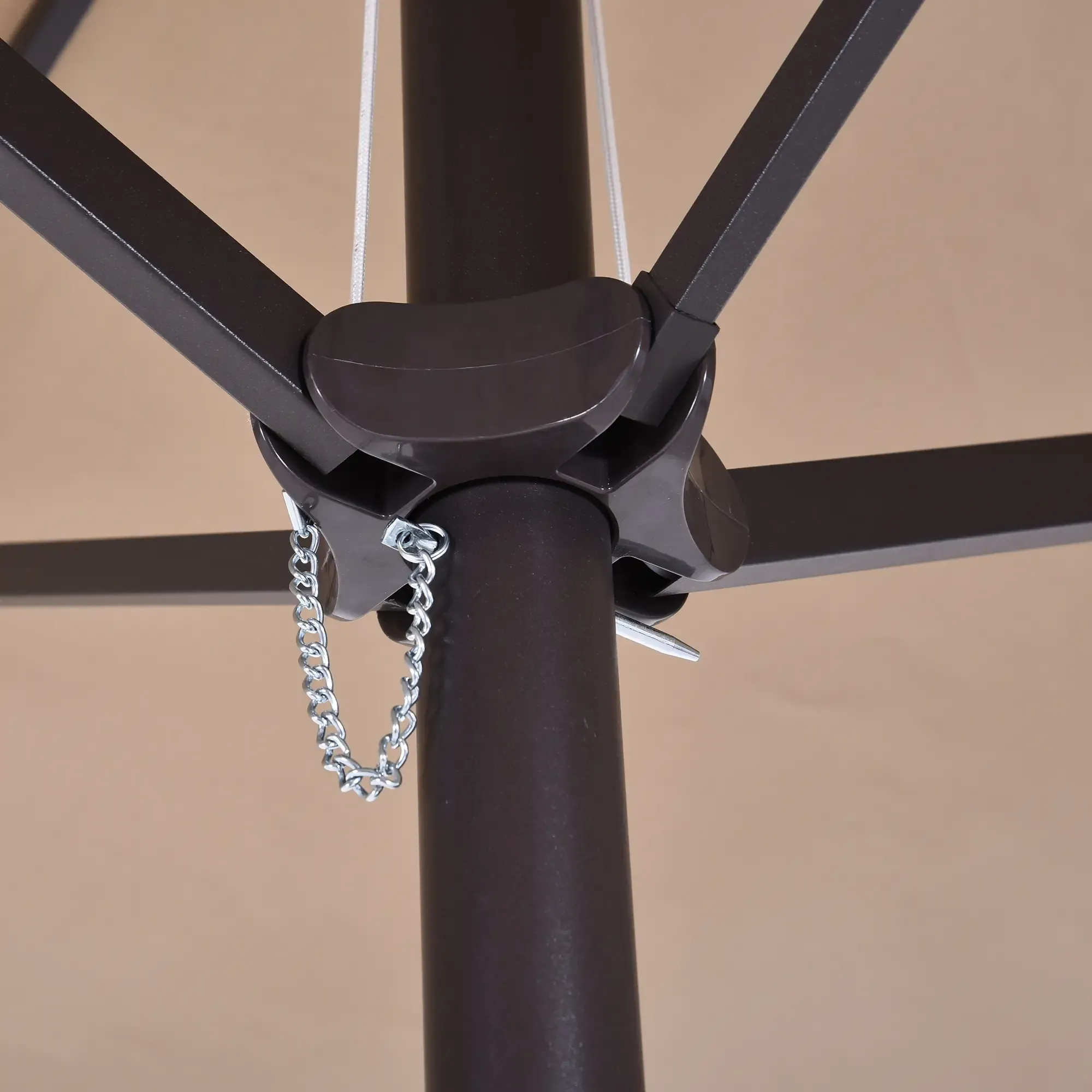 Nahaufnahme der Unterseite eines beigen Terrassenschirms, die das schwarze Gestell und eine kleine silberne Kette zeigt.