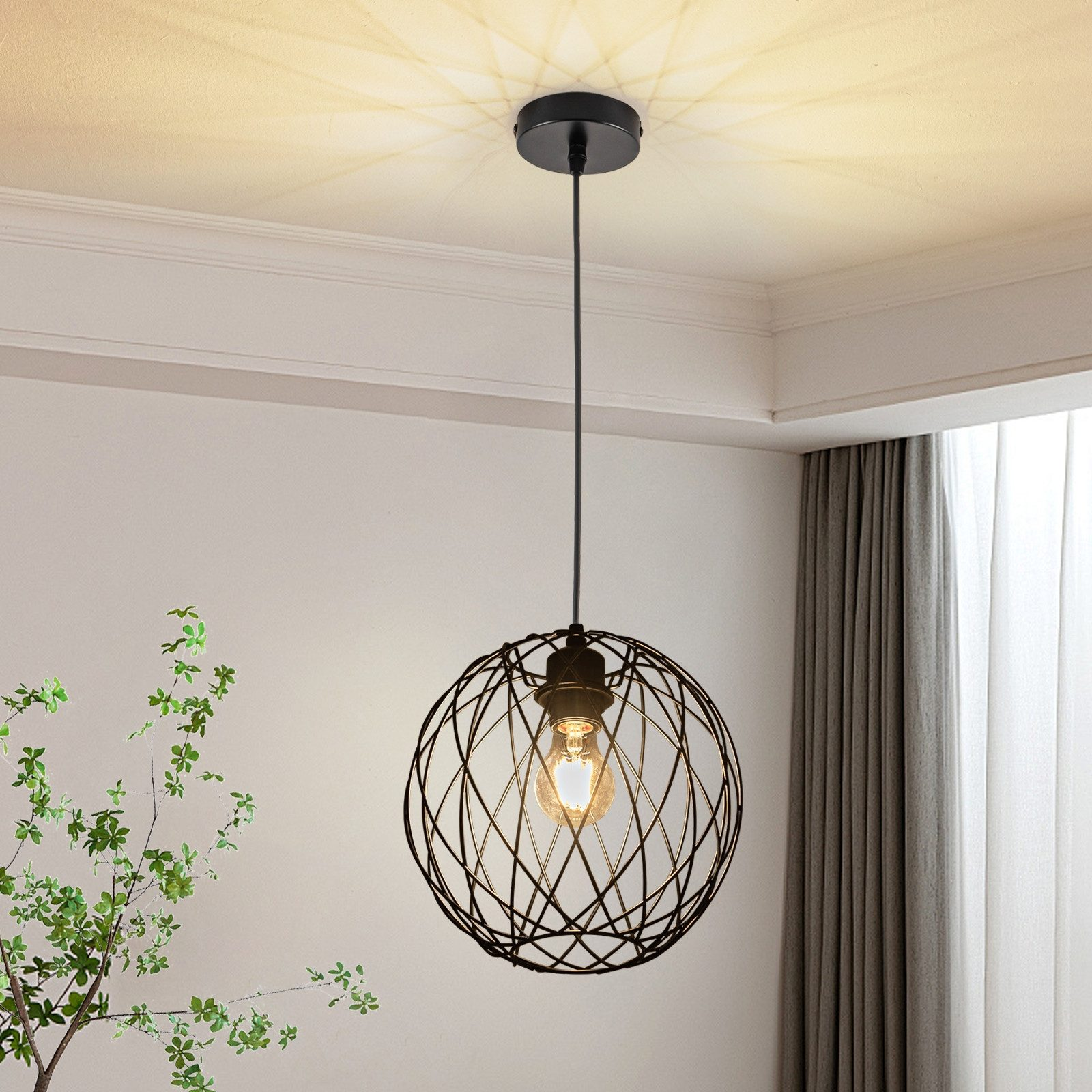 Una moderna lampada a sospensione con gabbia in metallo nero pende dal soffitto con una pianta verde fogliosa sulla sinistra.