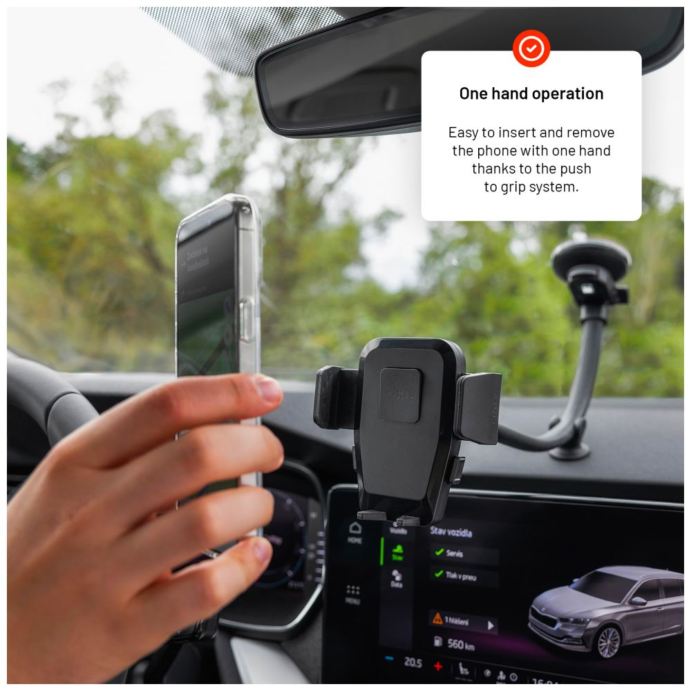 Eine Hand legt ein Telefon in eine schwarze Autohalterung. Das Armaturenbrett des Autos und Grün sind sichtbar.
