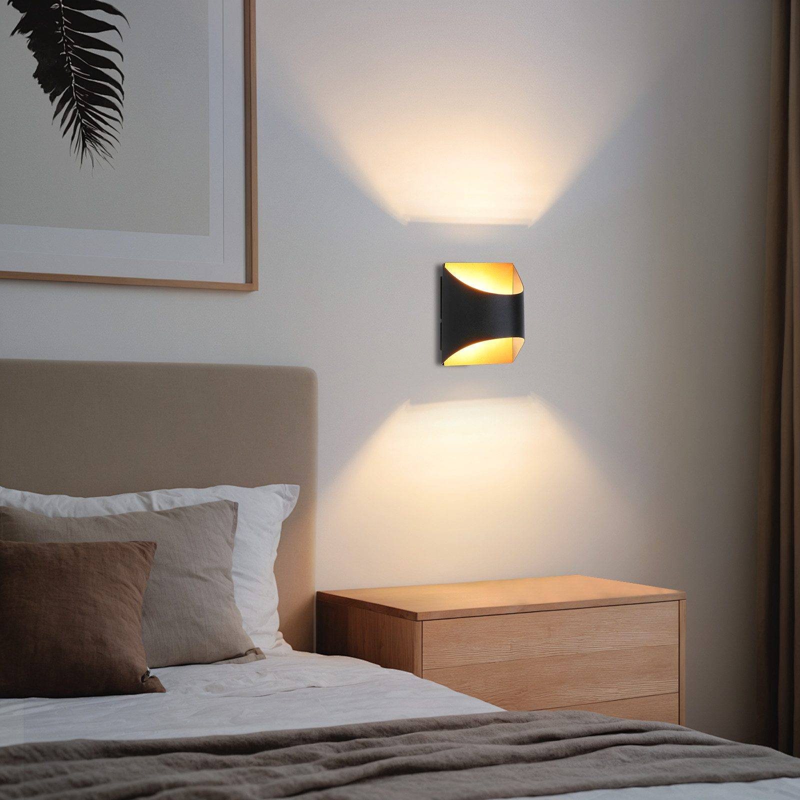 Una lampada da parete curva nera e oro illumina una camera da letto con un letto, un comodino e opere d'arte incorniciate.