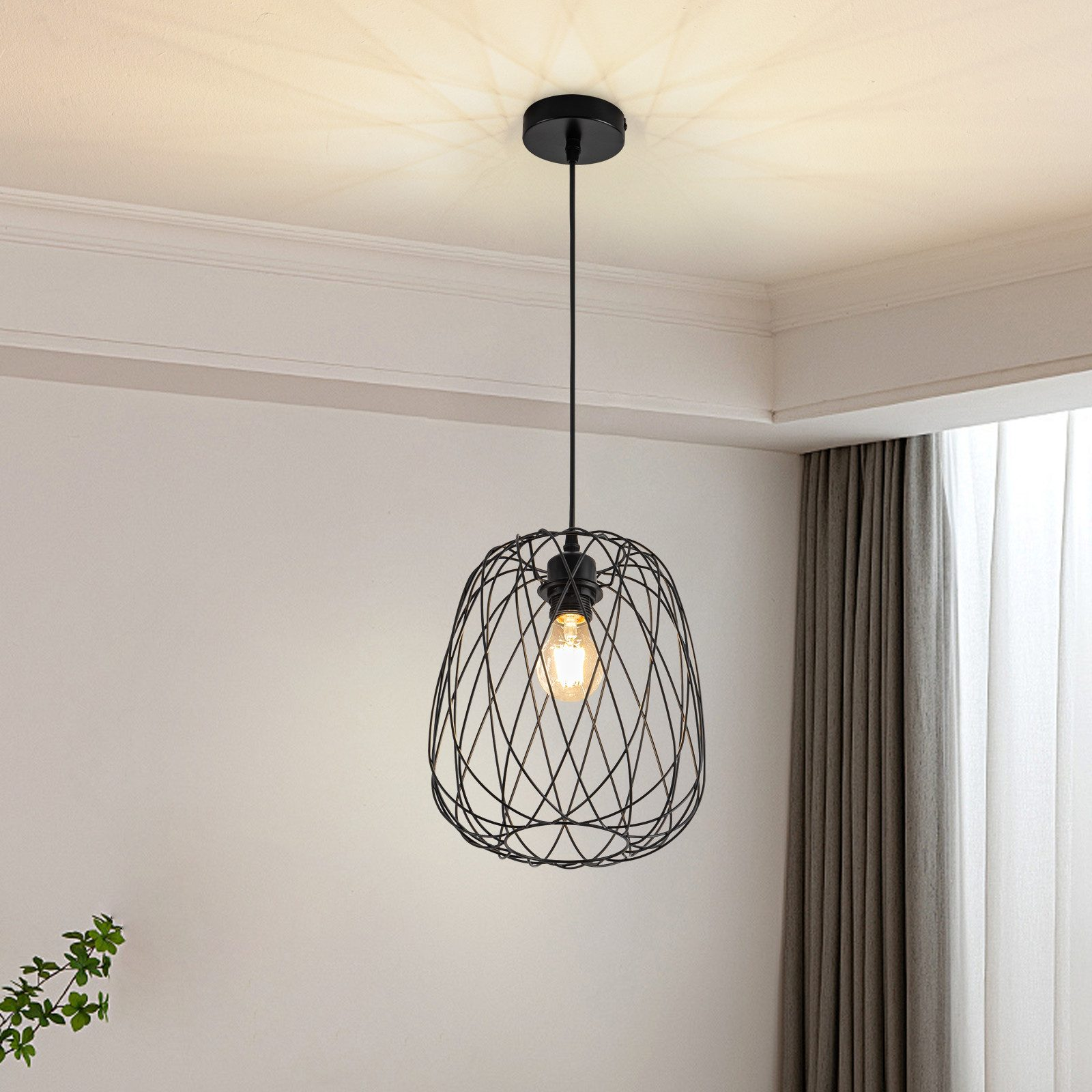 Una lampada a sospensione in filo metallico pende in un angolo con pareti bianche, completando una tenda e una pianta.