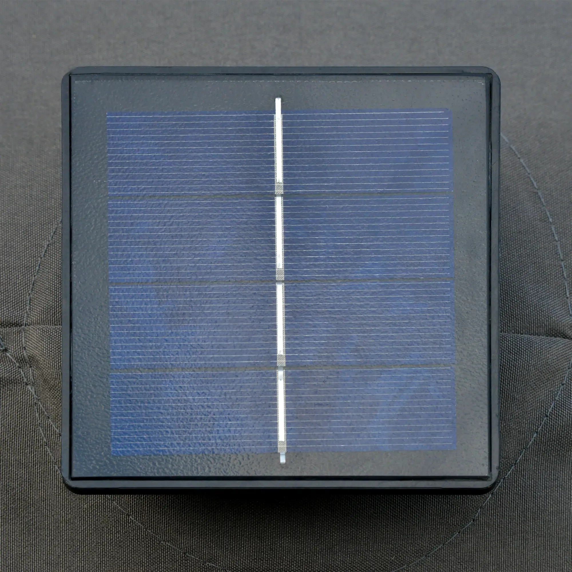 Ein schwarzes quadratisches Solarpanel auf einer grauen Oberfläche.