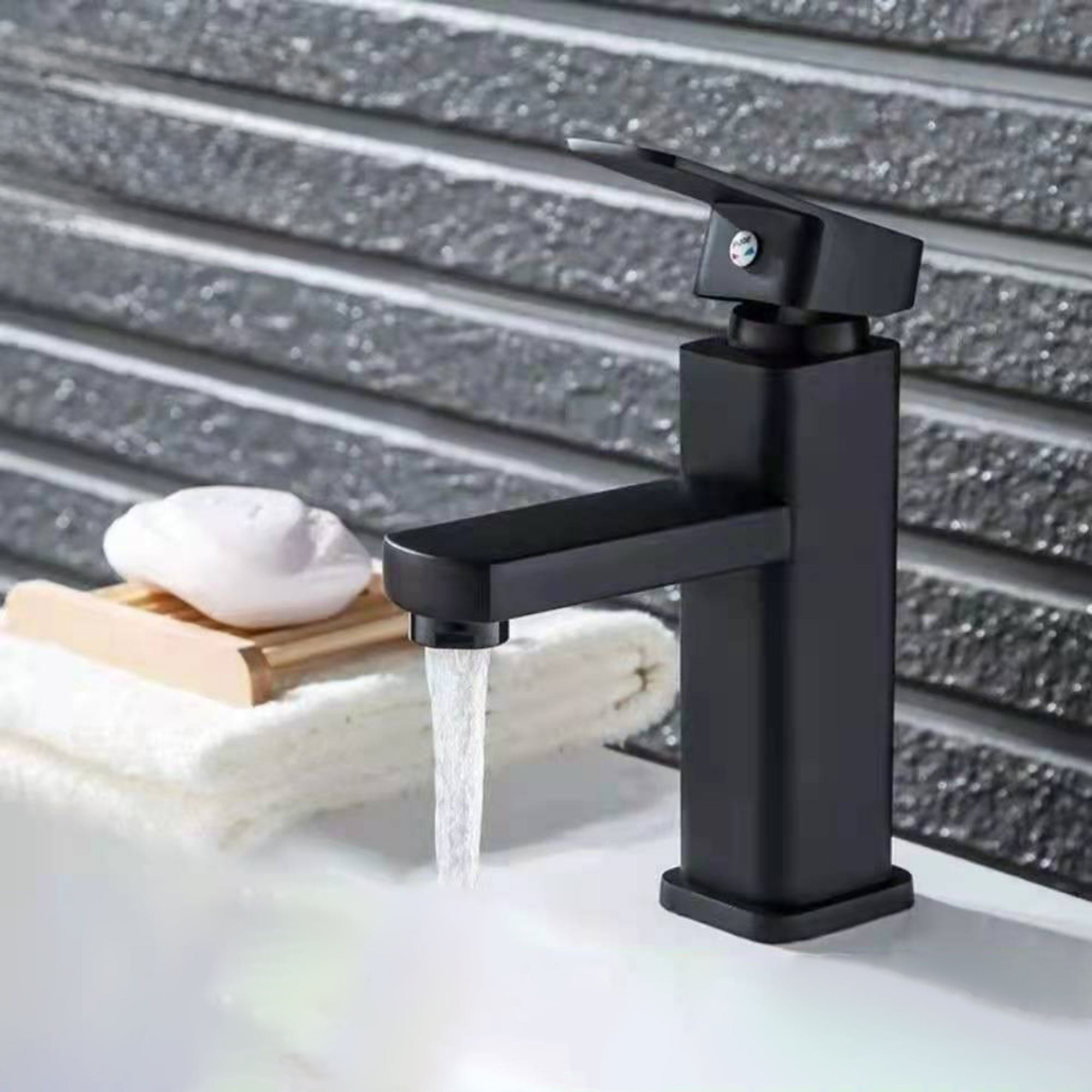 Schwarzer Wasserhahn mit fließendem Wasser, Seife und Handtuch im Hintergrund.