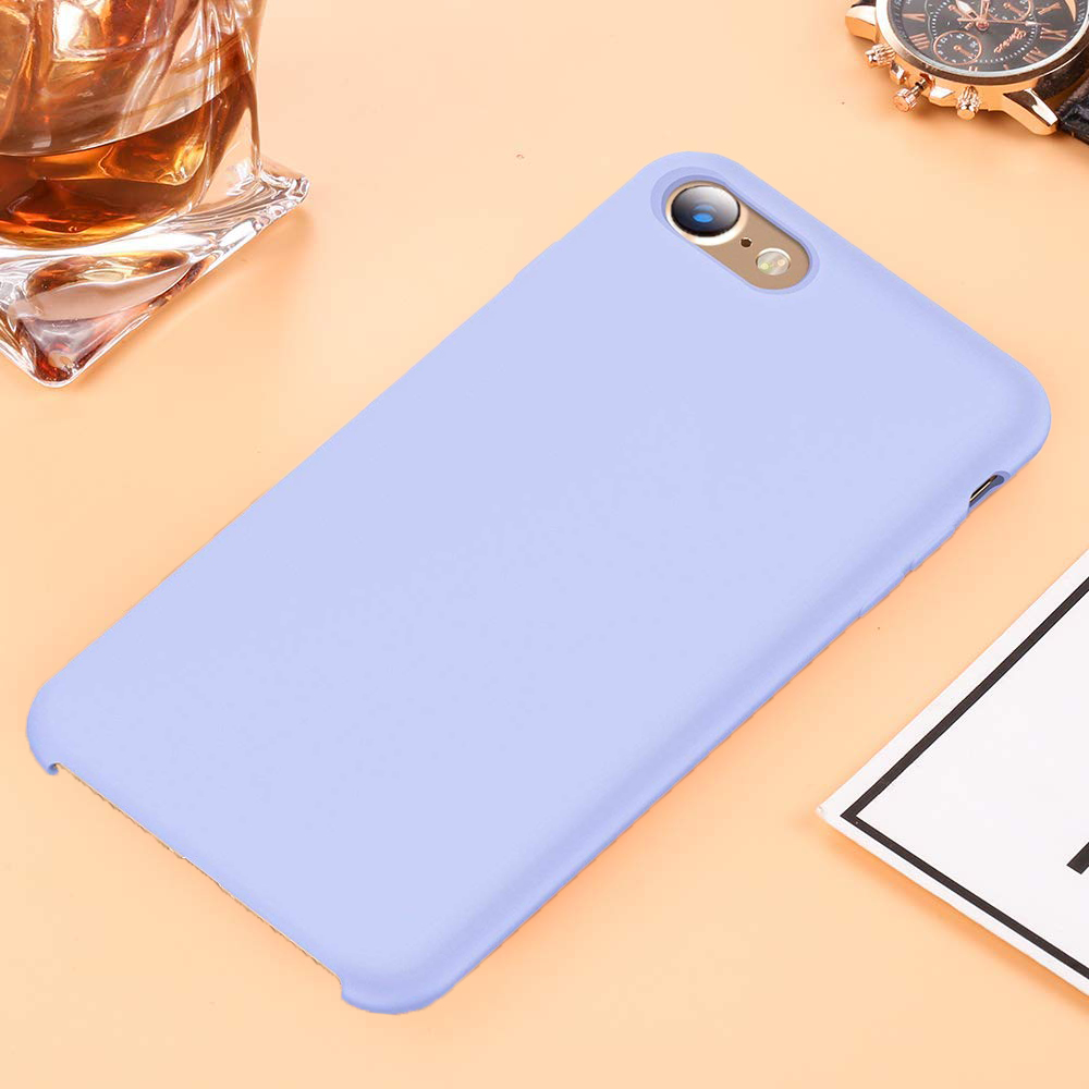 Eine hellviolette Telefonhülle neben einem Telefon. Ein Glas Flüssigkeit und eine Uhr sind im Hintergrund.