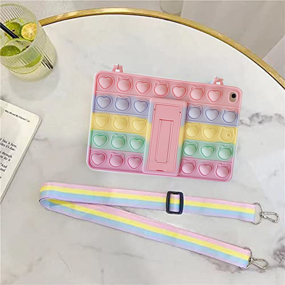 Pastellfarbene Pop-it-iPad-Hülle mit Herzen und Bären, zusammen mit einem Regenbogenband und einem Getränk auf einem Marmortisch.
