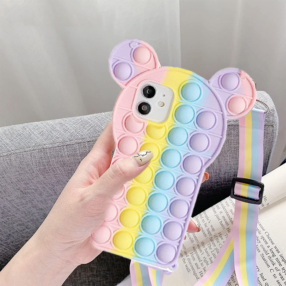 Hand hält eine pastellfarbene Regenbogen-Bubble-Pop-Handyhülle mit einem Riemen auf einer grauen Couch.