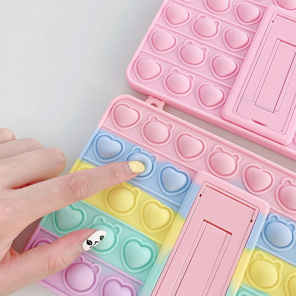 Hand drückt auf eine pastellfarbene Bubble-Pop-iPad-Hülle mit einem faltbaren Ständer auf einem weißen Hintergrund.