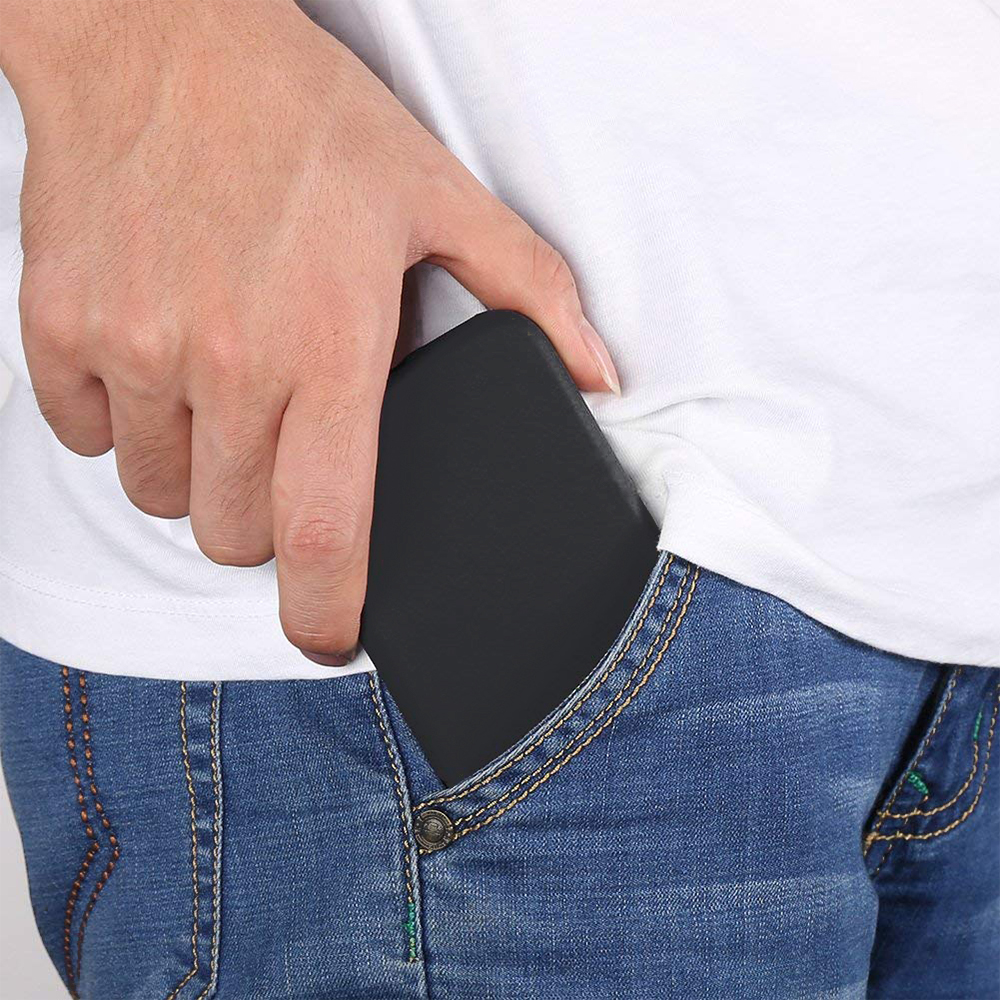 Die Hand einer Person steckt ein schwarzes Telefon in die blaue Jeanshosentasche. Die Person trägt ein weißes T-Shirt.