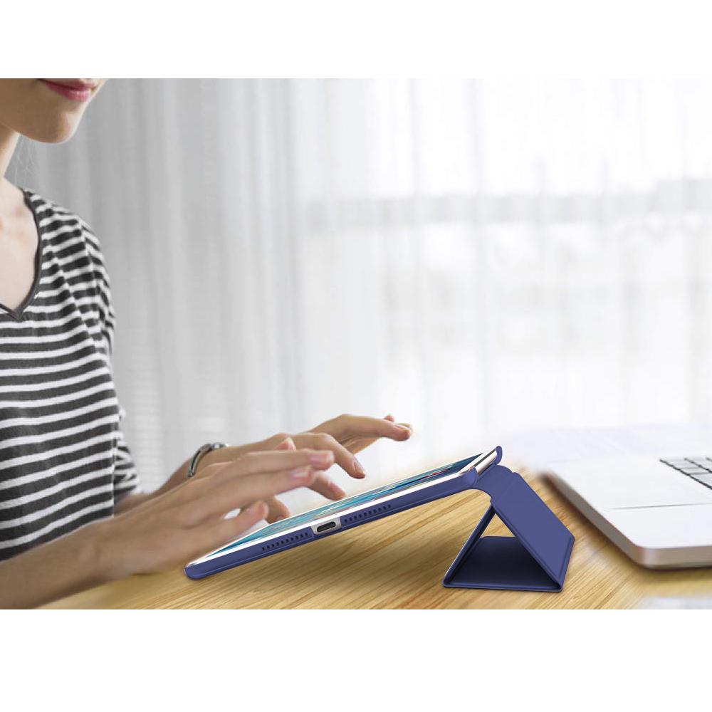 Person benutzt ein blaues iPad in einer Klapphülle auf einem Schreibtisch mit einem Laptop im Hintergrund.
