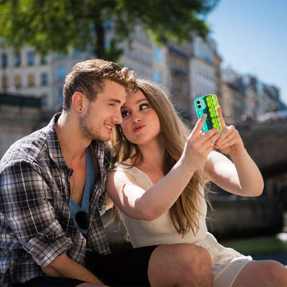 Ein Paar posiert für ein Selfie mit einer Handyhülle vor einem Stadtbild. Die Hülle hat ein farbenfrohes Design.