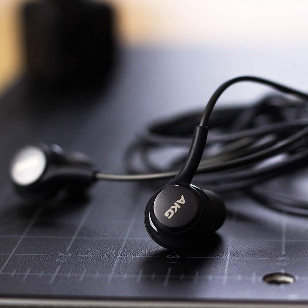 Schwarze AKG-Ohrhörer auf dunkler Oberfläche. Der rechte Ohrhörer ist fokussiert, mit dem AKG-Logo.