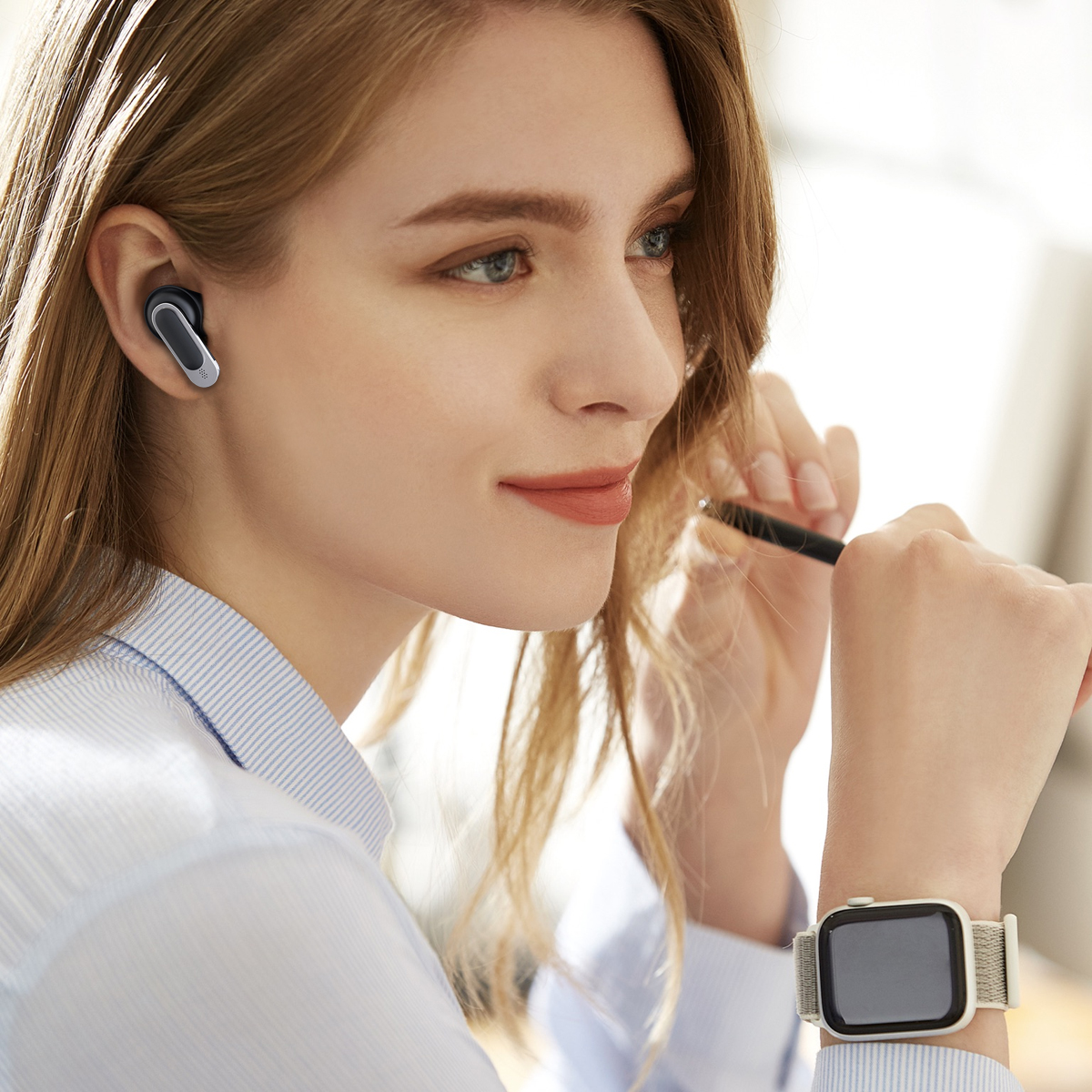 Eine Frau, die einen grauen und silbernen Ohrhörer und eine Smartwatch trägt.