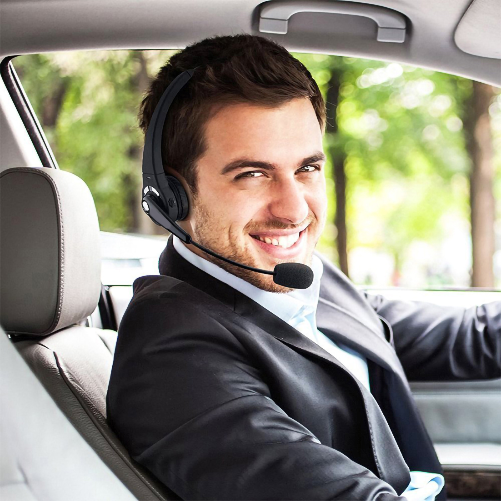 Ein Mann im Anzug, der ein schwarzes drahtloses Headset in einem Auto trägt.